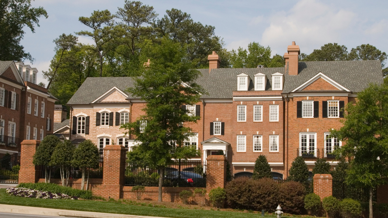 Row of red-brick houses with white trim and trees along a quiet street