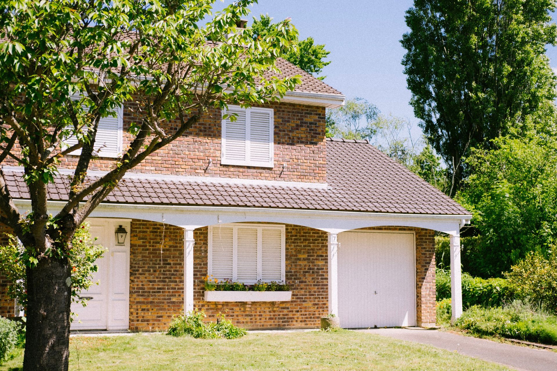 Two-story brick house with white shutters, garage, and trees in the front yard