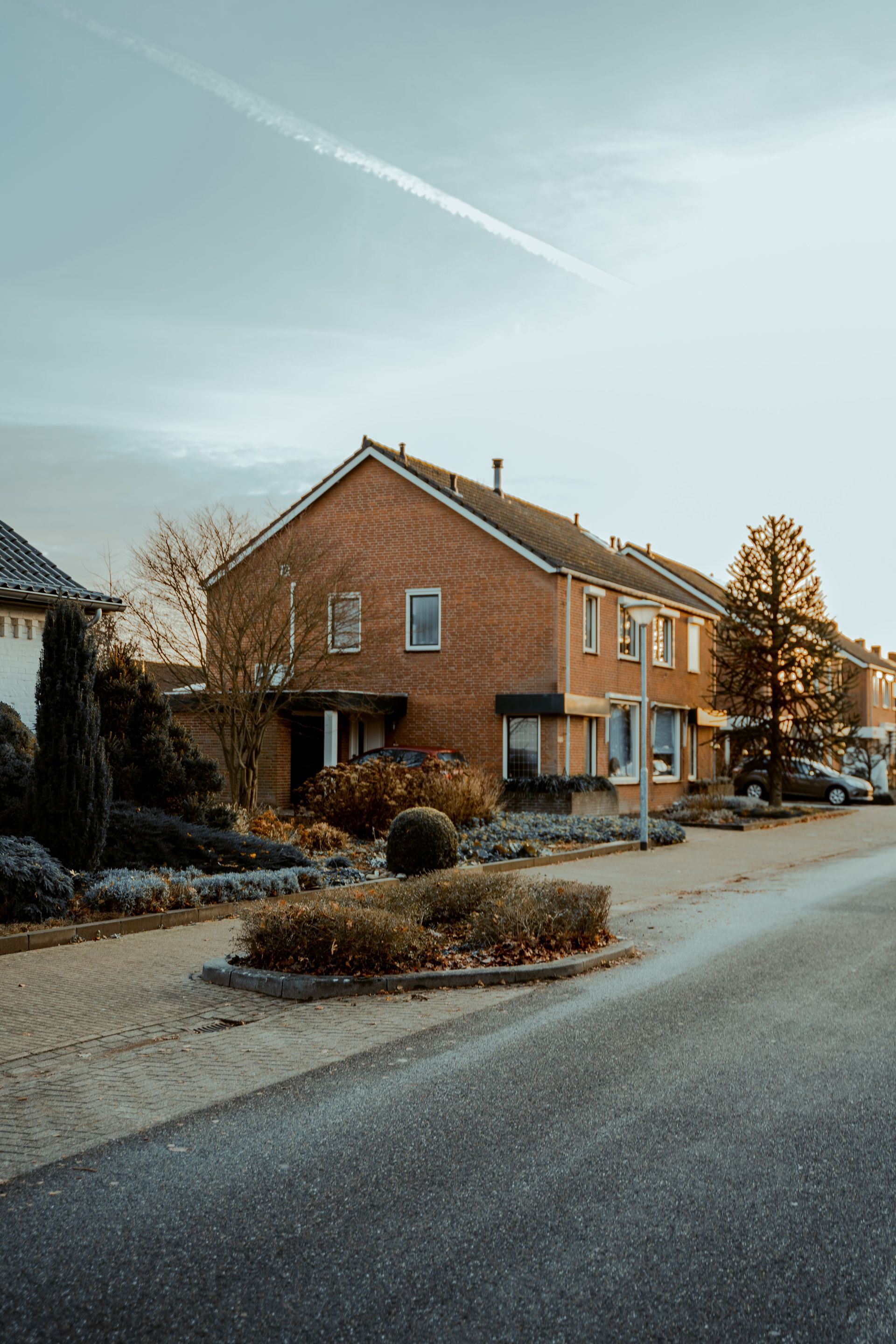 Brick houses on a quiet suburban street with bare shrubs and a frosty road under a pale sky