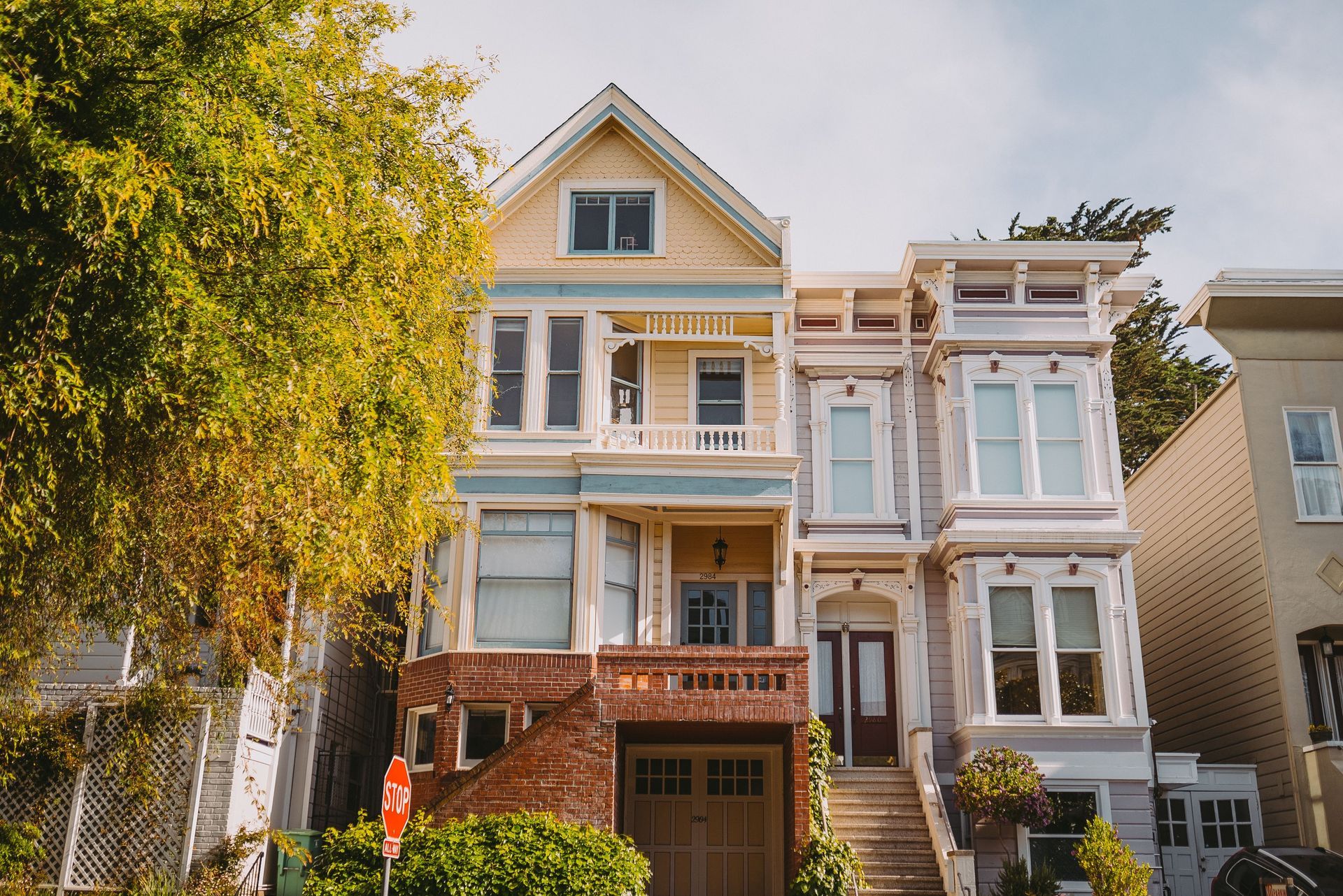 Two Victorian houses with ornate facades and a leafy tree in front