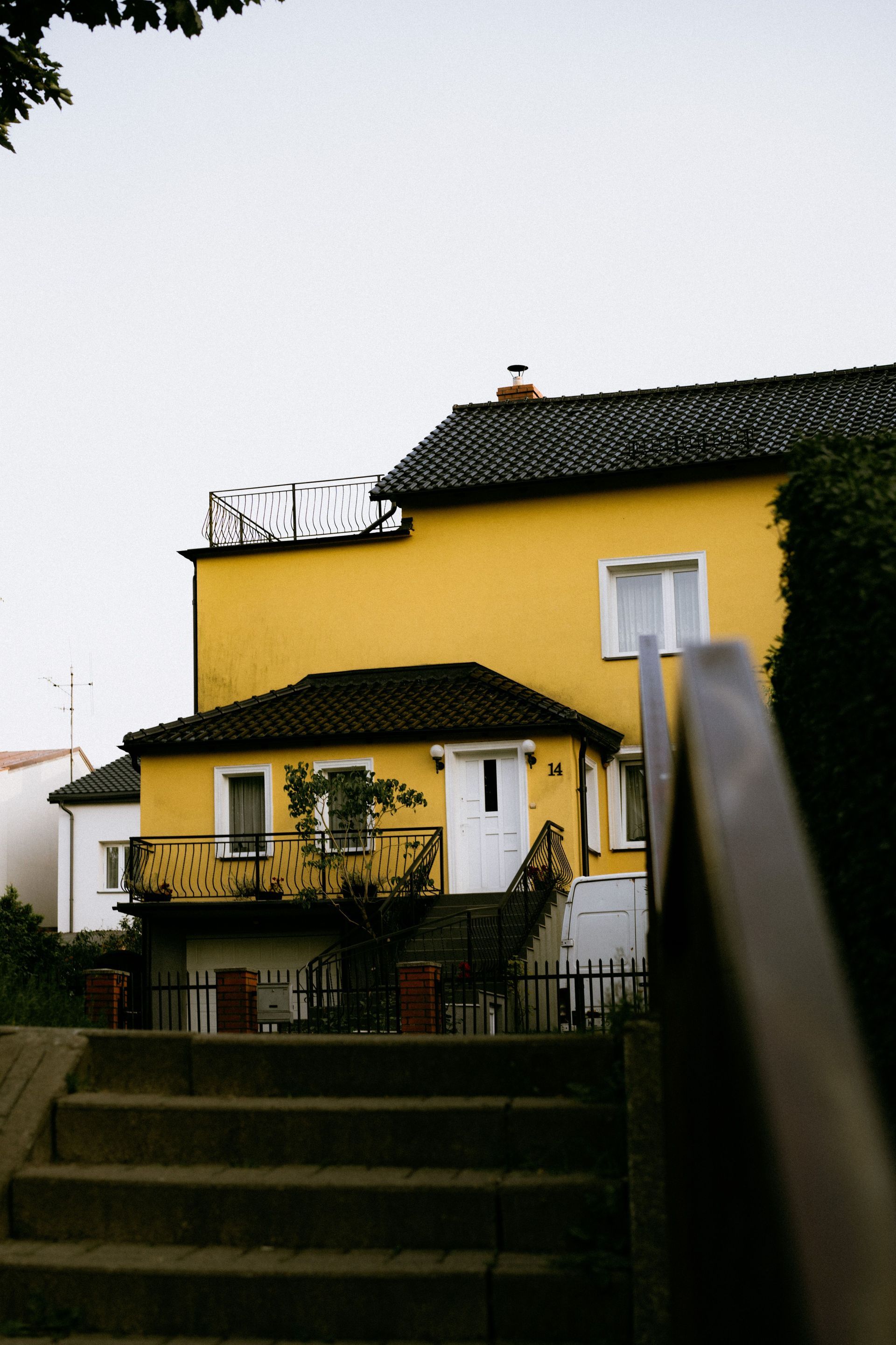 Yellow house with dark roof and stairs in the foreground on an overcast day