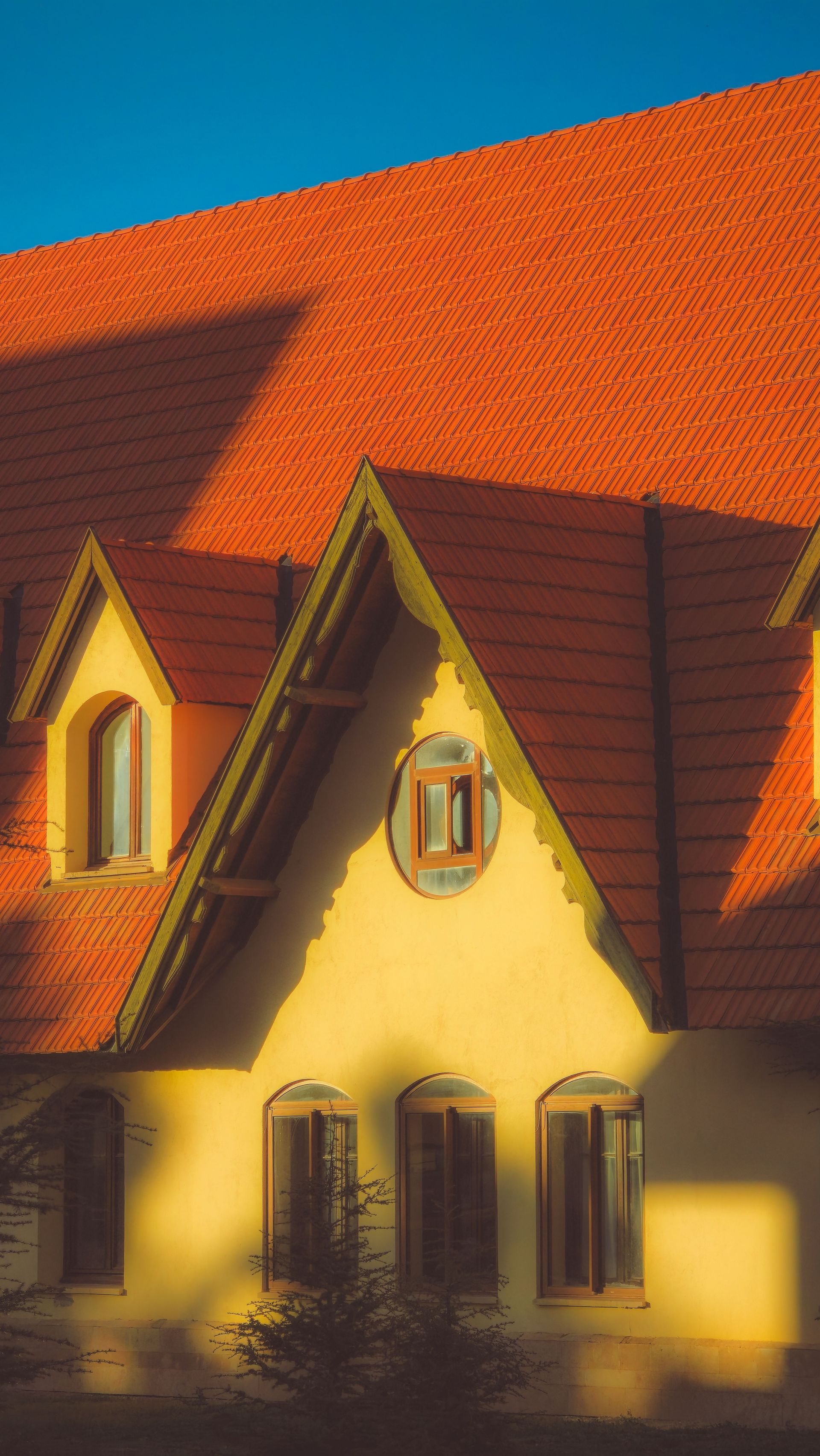 Yellow house with steep red roof and dormer windows in warm sunlight