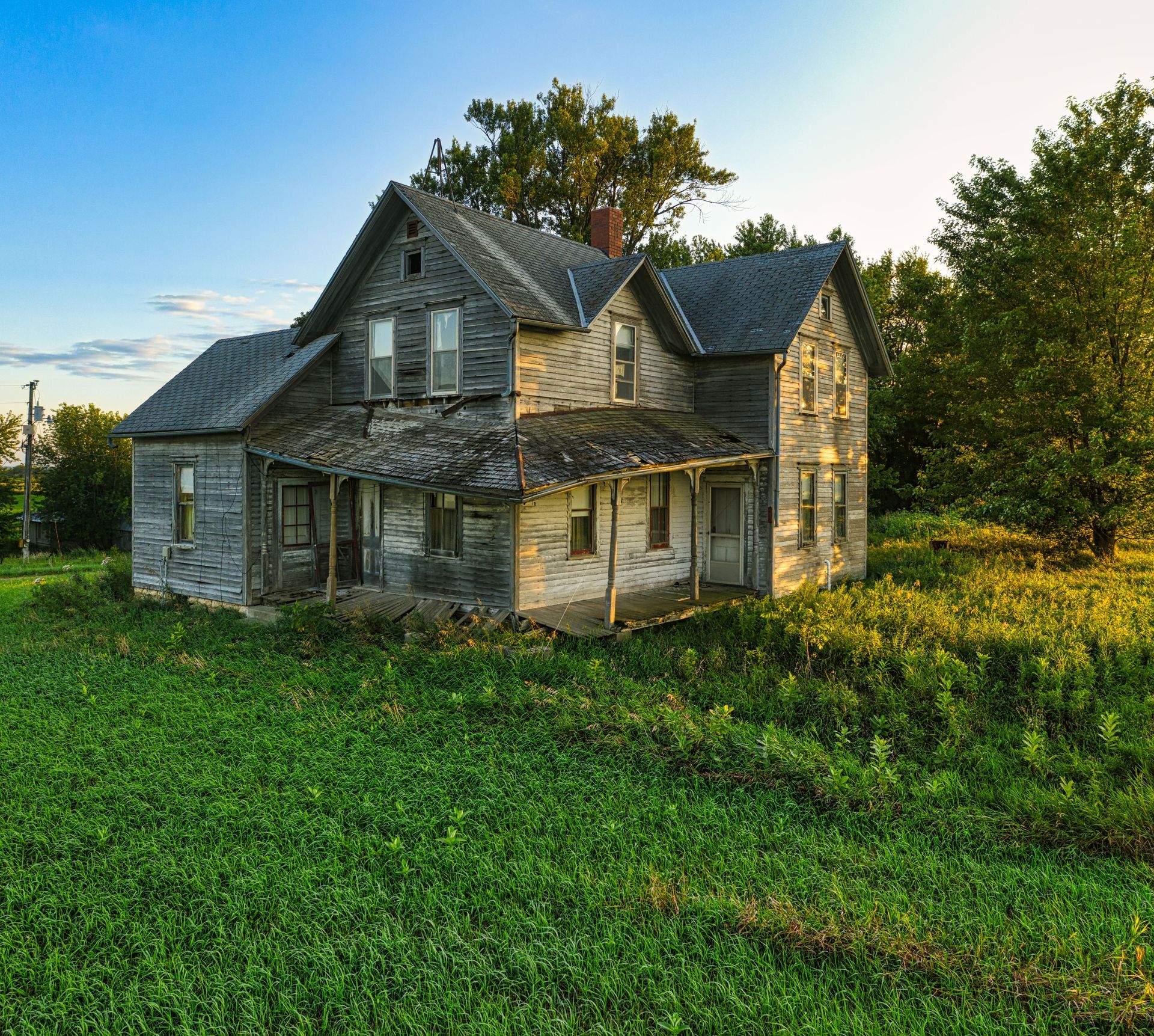 Old stone farmhouse with a weathered roof sits in a green field at sunset.