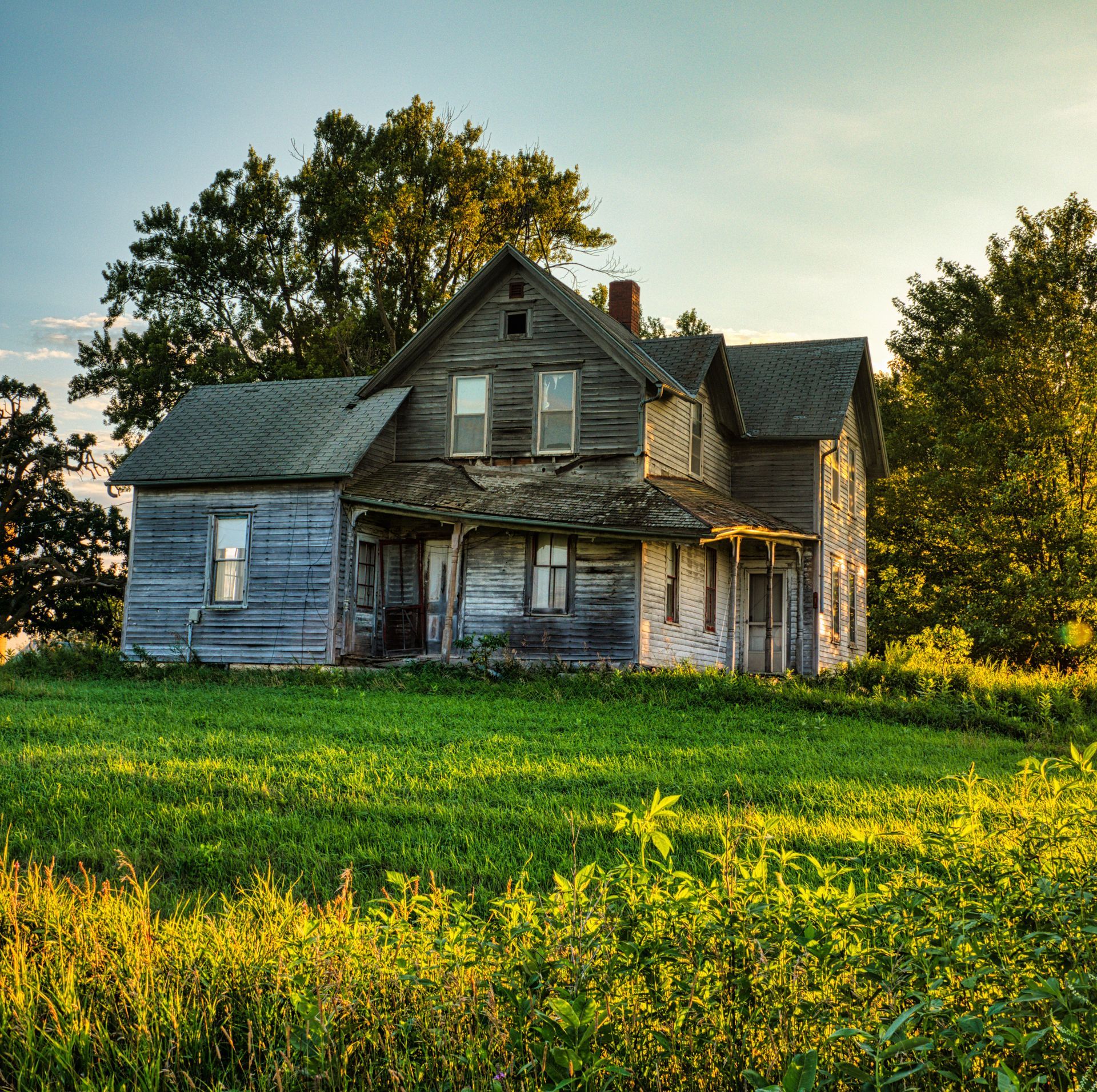 Abandoned weathered farmhouse beside a green field at sunset