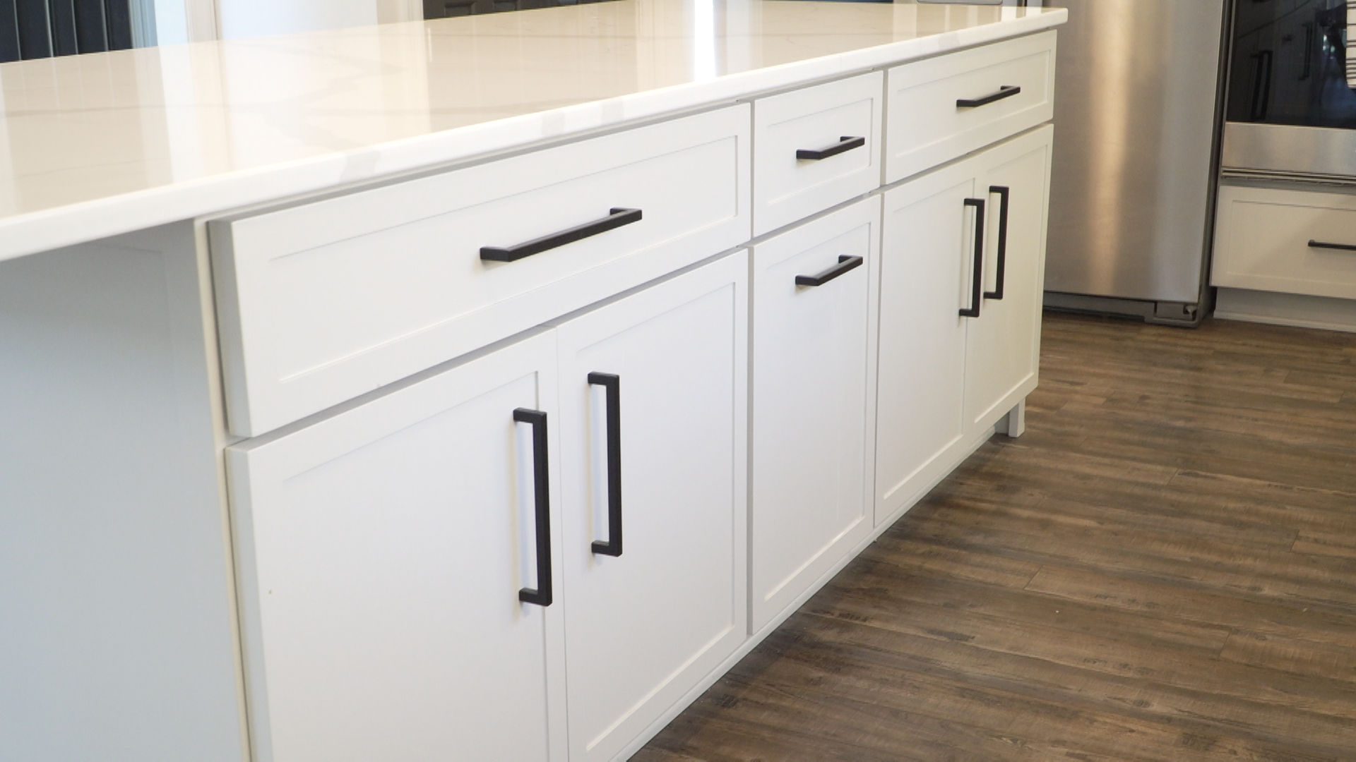 White kitchen cabinets with black handles and a wood floor beneath a light countertop.