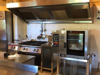 Cucina professionale con piano cottura, forno e ampia cappa aspirante in acciaio inox sopra un bancone di preparazione.