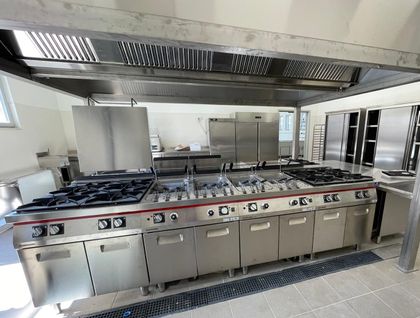 Cucina professionale da ristorante in acciaio inox con fornelli a gas, forni e grande cappa aspirante.