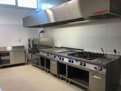 Cucina professionale con piano cottura in acciaio inox, ampia cappa aspirante e pareti piastrellate.
