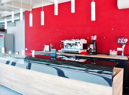 Bancone da bar moderno con parete rossa, lampade a sospensione bianche e vetrina per dolci.