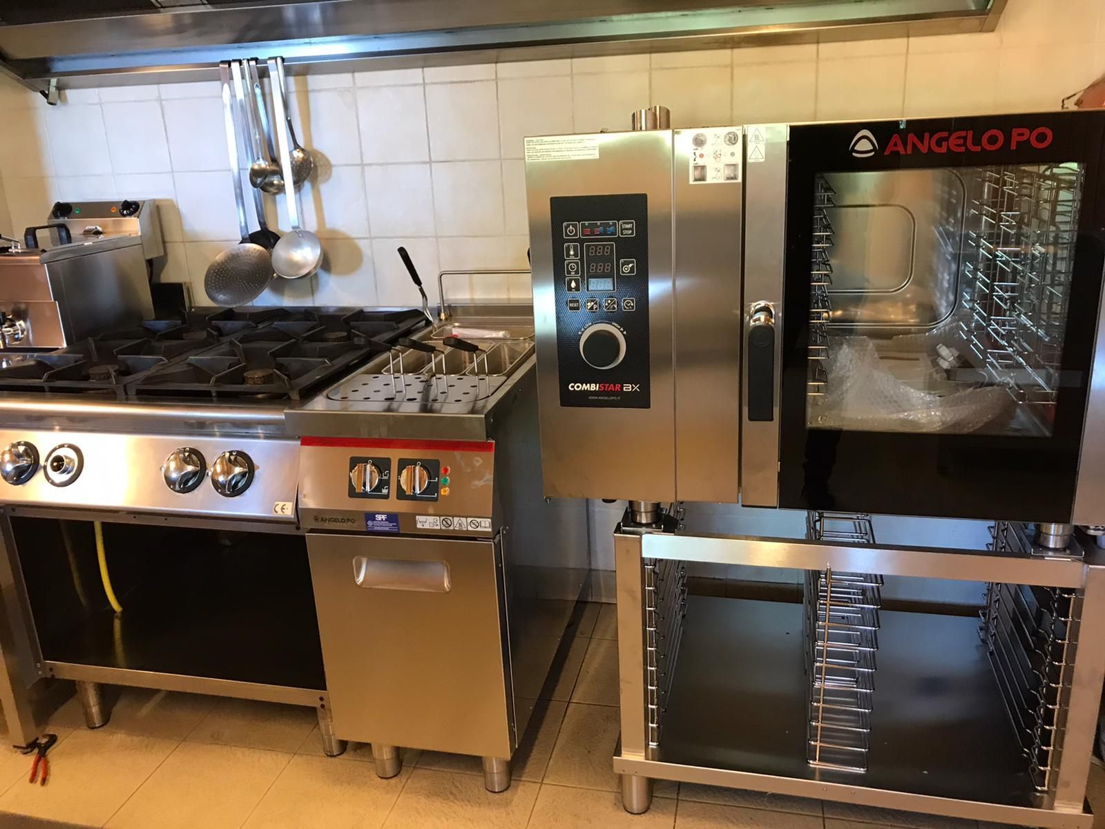 Cucina professionale con piano cottura, forno e forno a convezione in acciaio inox, addossata a una parete piastrellata.