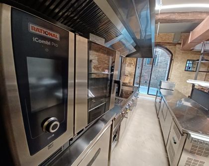Cucina professionale con forno combinato Rational in acciaio inox e bancone di preparazione lungo una parete in mattoni.