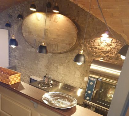 Bancone da cucina rustico con lampade a sospensione, parete in pietra, vassoio in metallo, lavello e forno sullo sfondo.