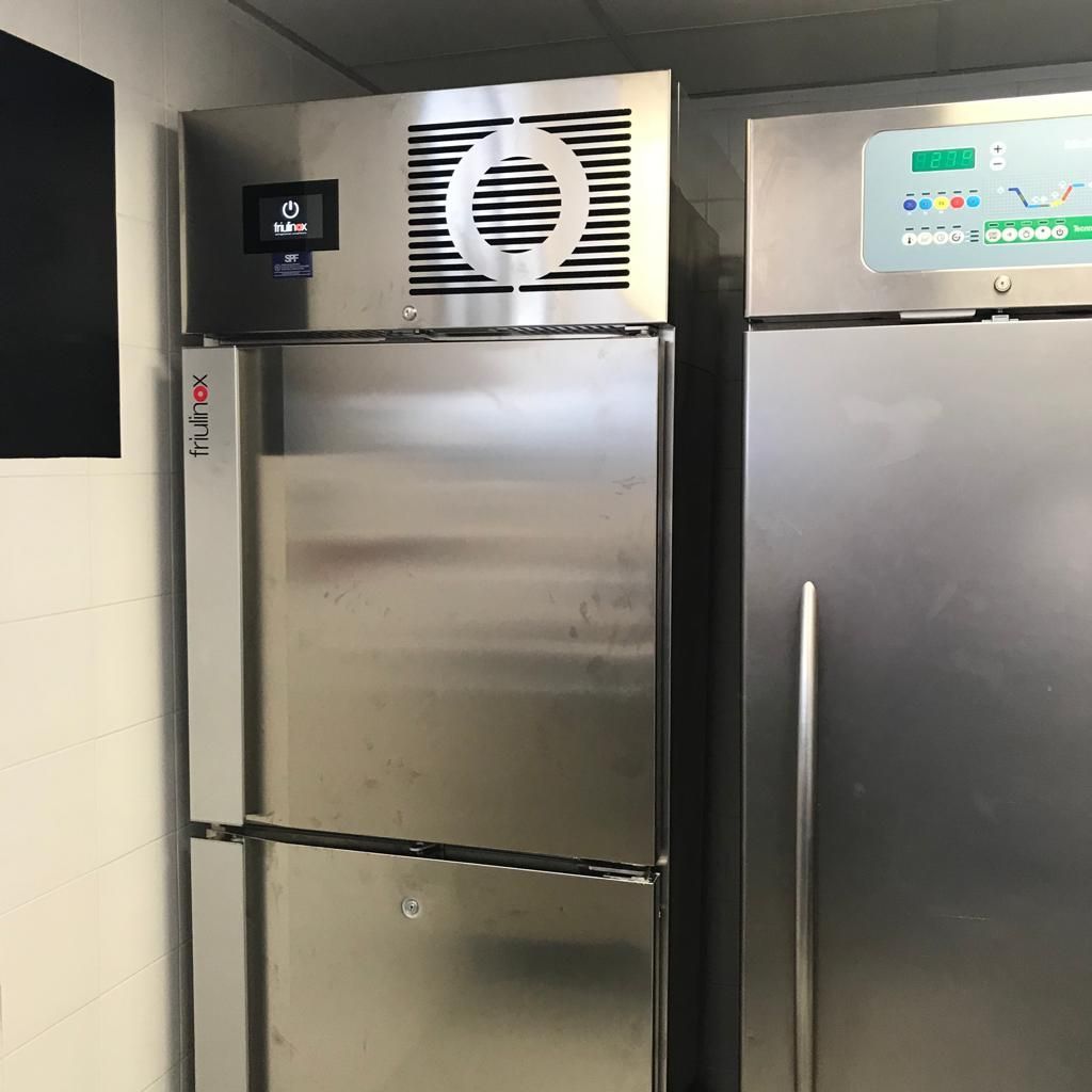 Frigoriferi commerciali in acciaio inox in una cucina, uno con ventola di aspirazione e uno con display digitale.