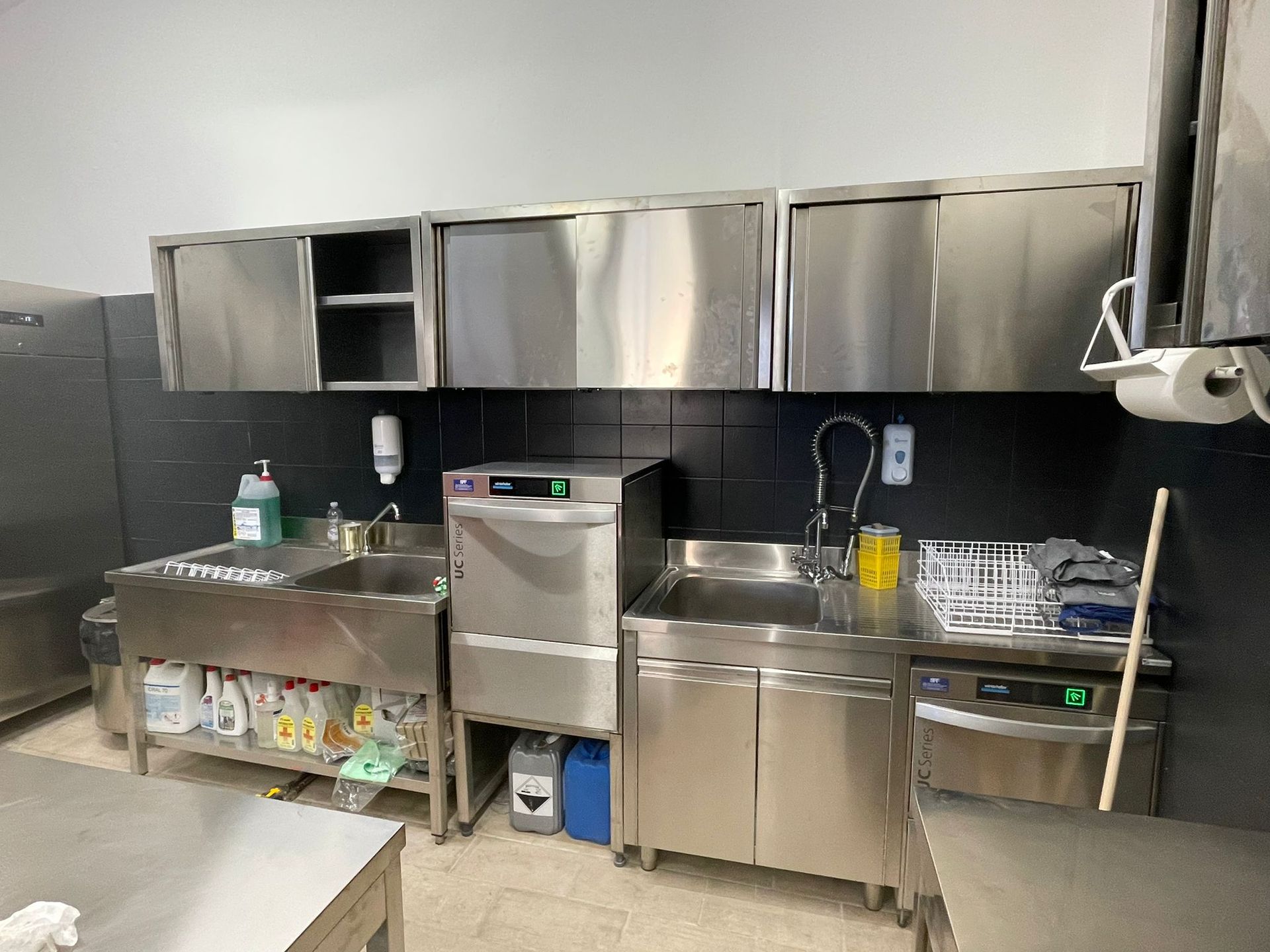Cucina professionale con mobili in acciaio inox, lavello, lavastoviglie e bancone per la preparazione degli alimenti.