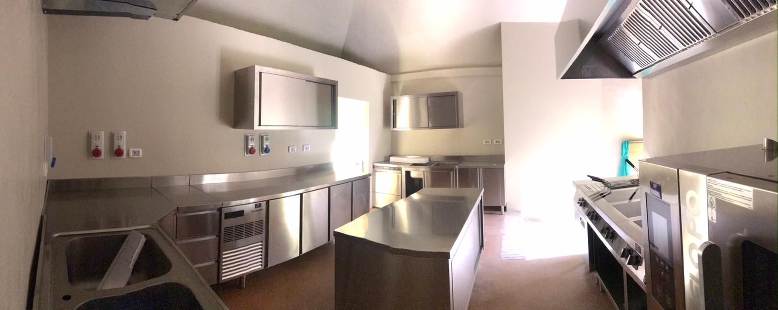 Cucina moderna e luminosa con elettrodomestici in acciaio inossidabile, mobili bianchi e isola centrale.