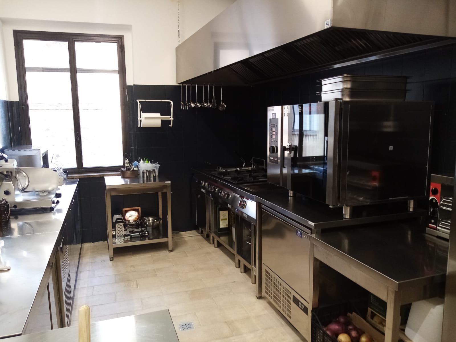 Cucina professionale con ripiani neri, elettrodomestici in acciaio inossidabile e un'ampia finestra