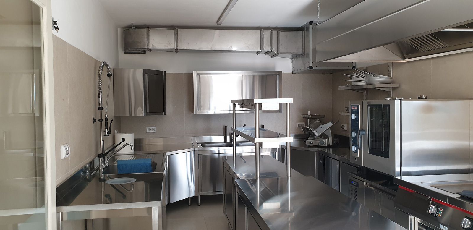 Cucina commerciale vuota in acciaio inox con banconi, lavelli, forni e cappe aspiranti.