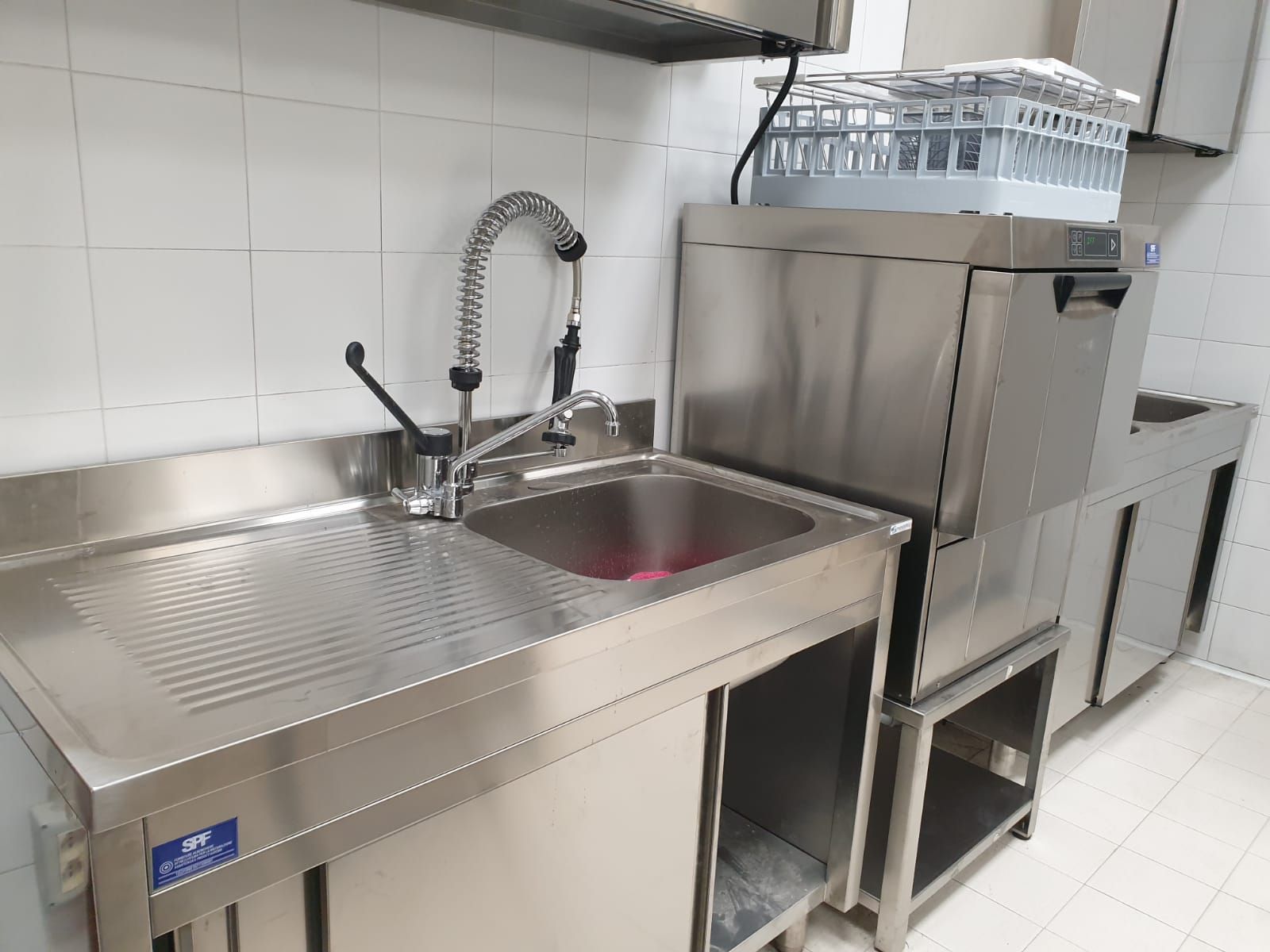 Lavello da cucina professionale in acciaio inox con doccetta estraibile e gocciolatoio, posizionato accanto a una lavastoviglie industriale.