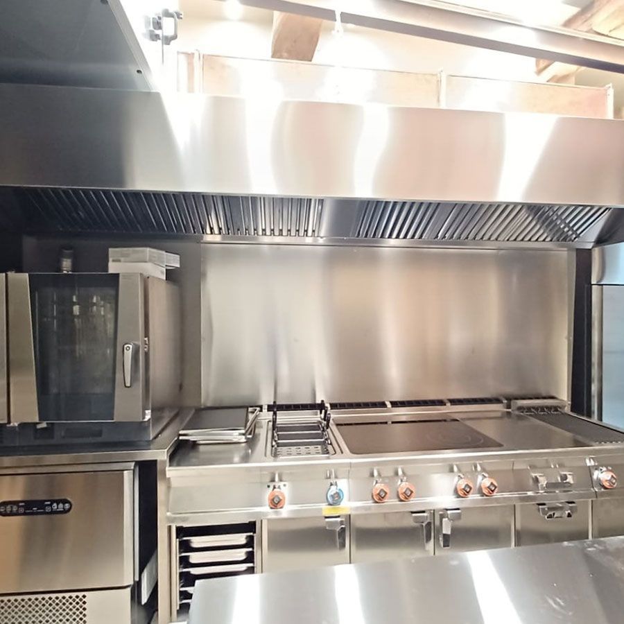 Cucina professionale in acciaio inox con piano cottura, griglia, friggitrice e cappa aspirante.