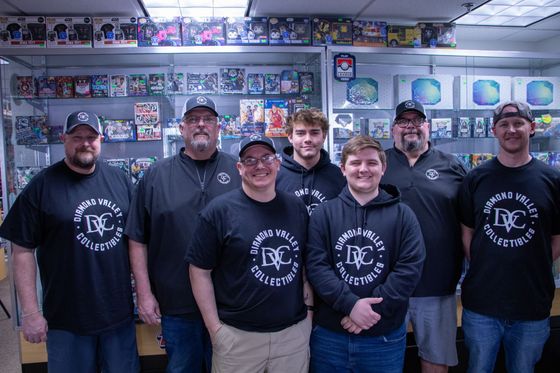 Six people in black logo T-shirts posing in a sports memorabilia shop