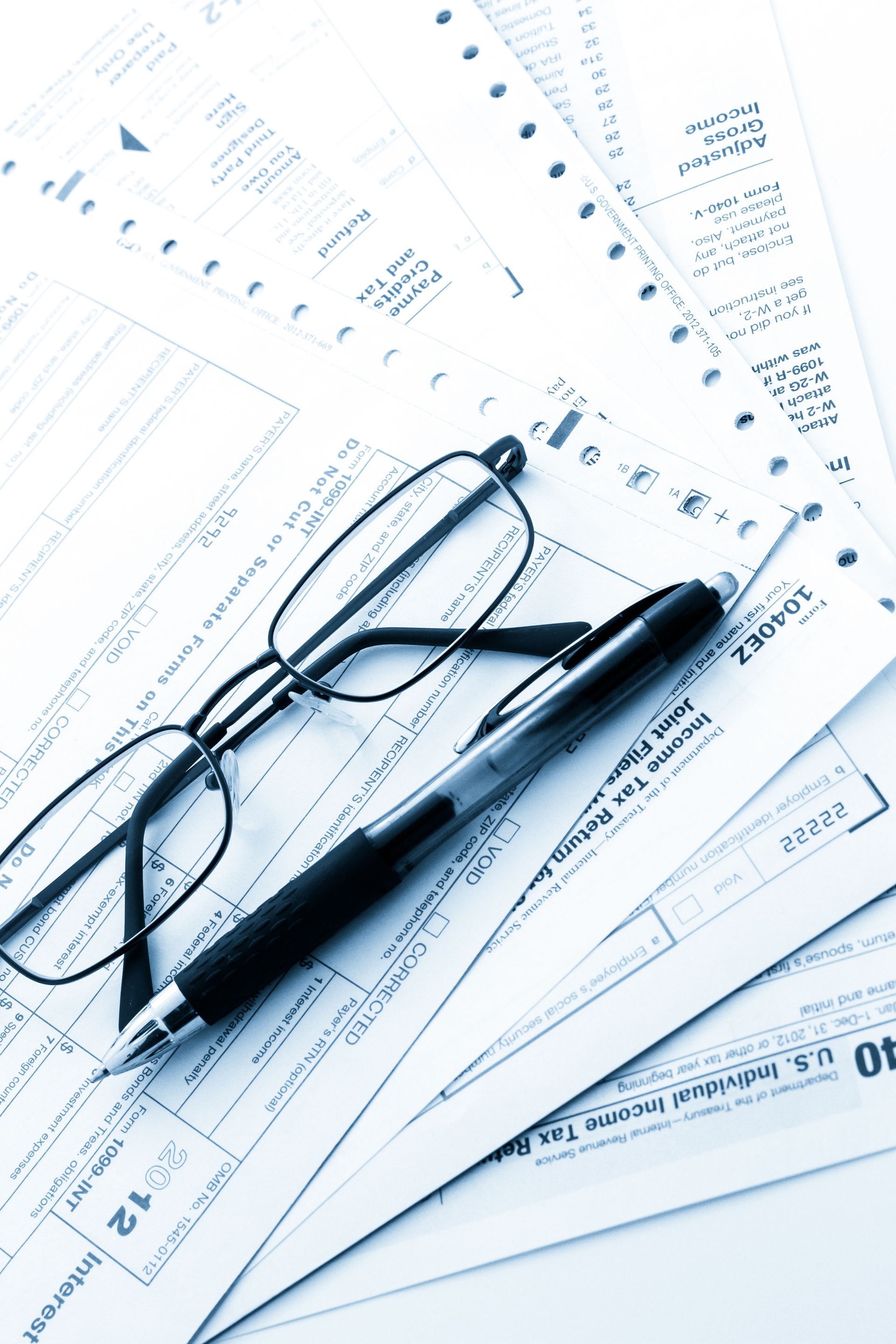 Glasses and pen resting on stacks of tax forms.
