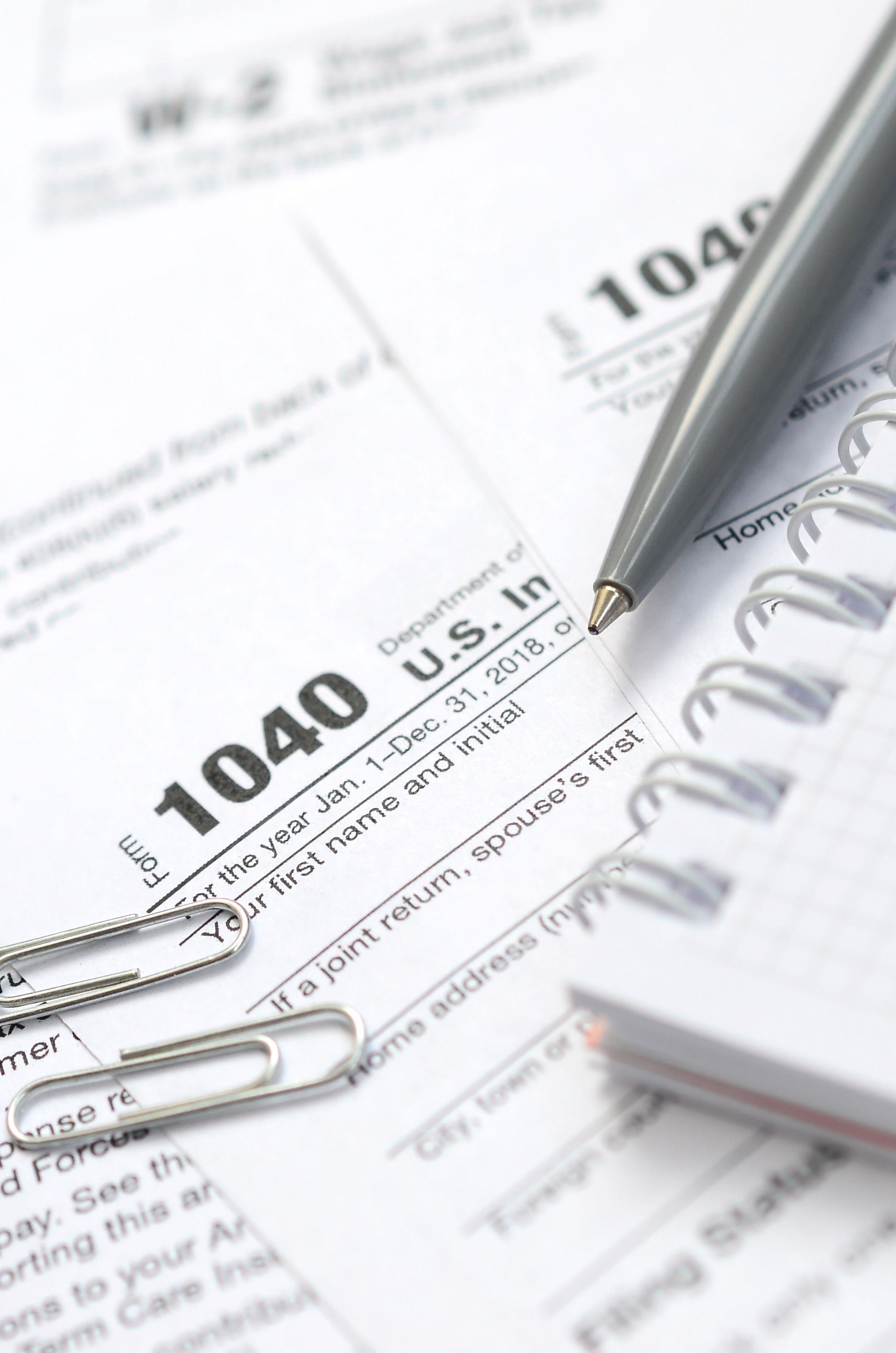 Tax forms, pen, paperclip, and notepad on a desk.