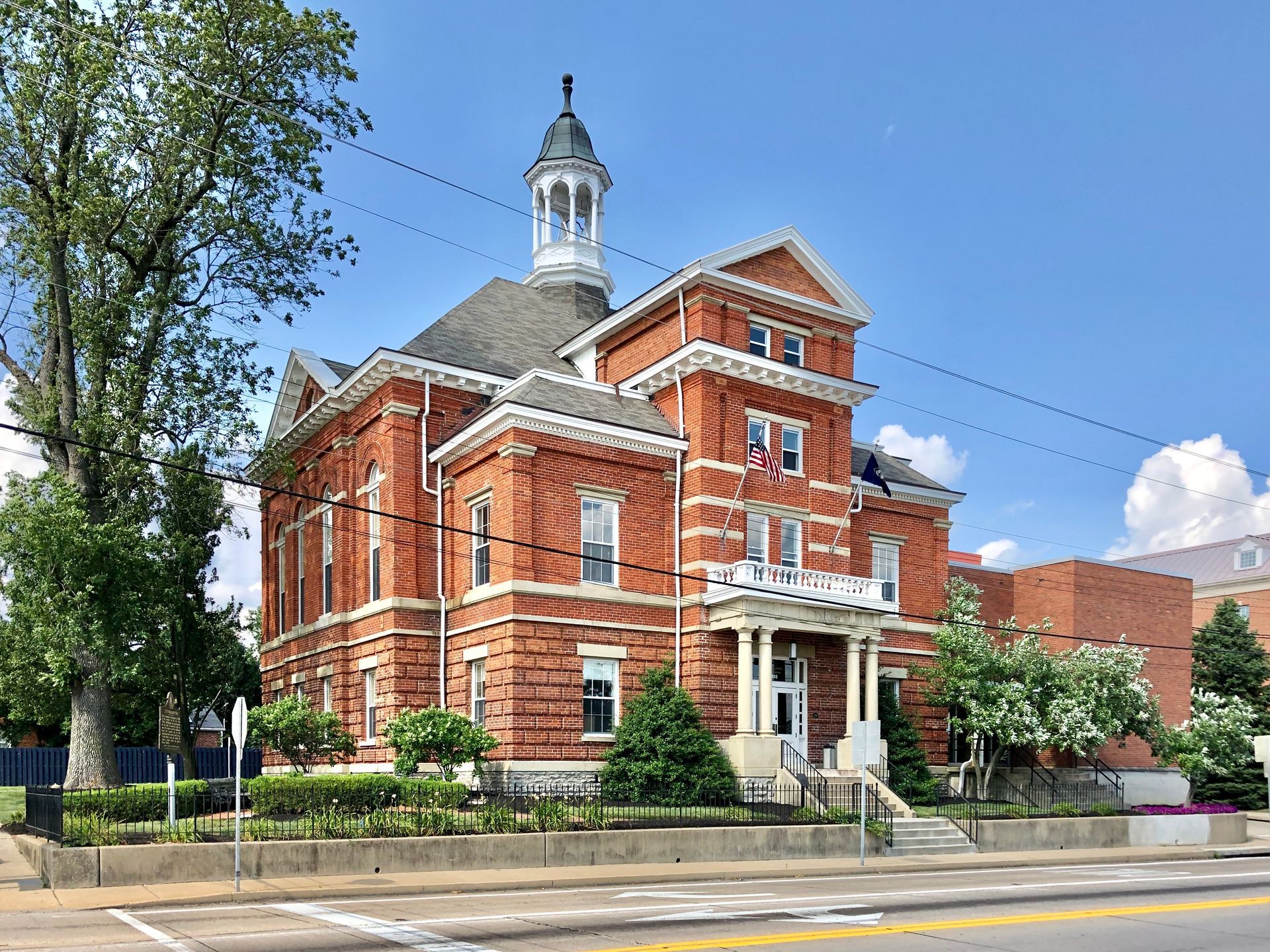 Brick courthouse with white trim, cupola, and American flag on a sunny day.