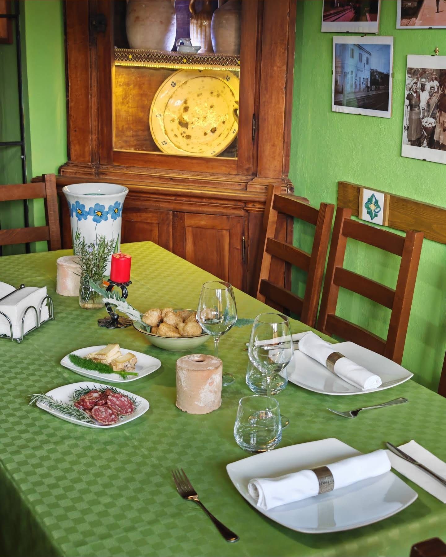 Apparecchiate la tavola con piatti, bicchieri, pane, formaggio e vino in una stanza accogliente con pareti verdi.
