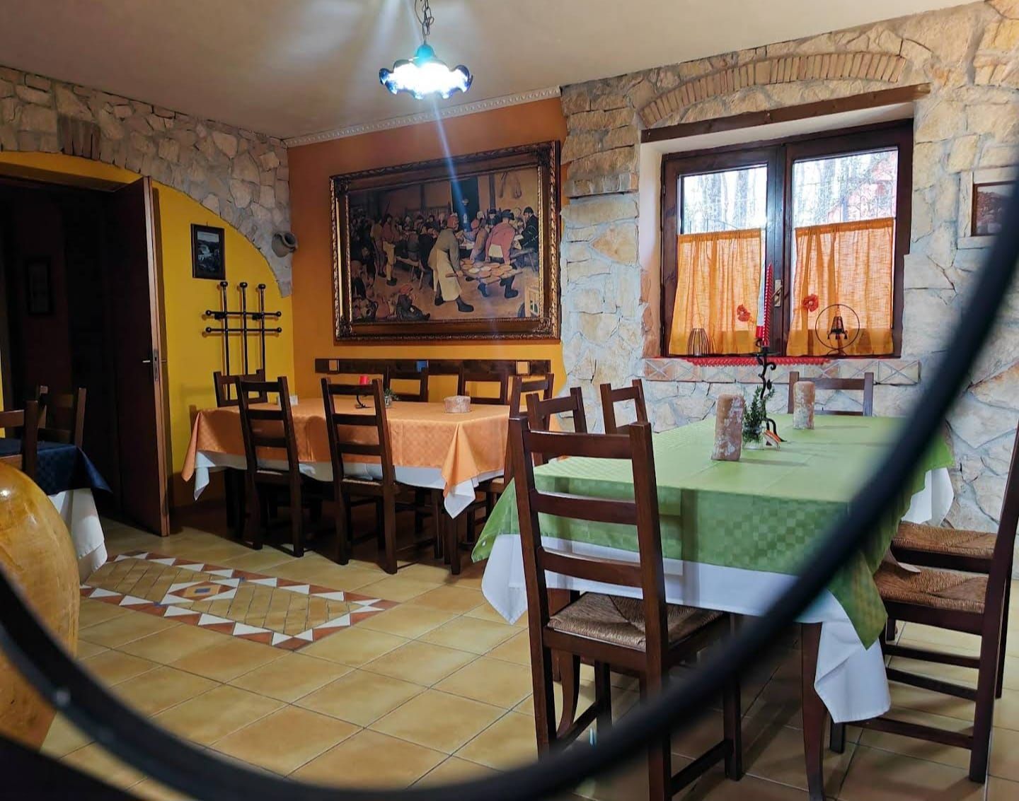 Accogliente sala da pranzo con tavoli in legno, tovaglie verdi, pareti in pietra e una finestra con tende.