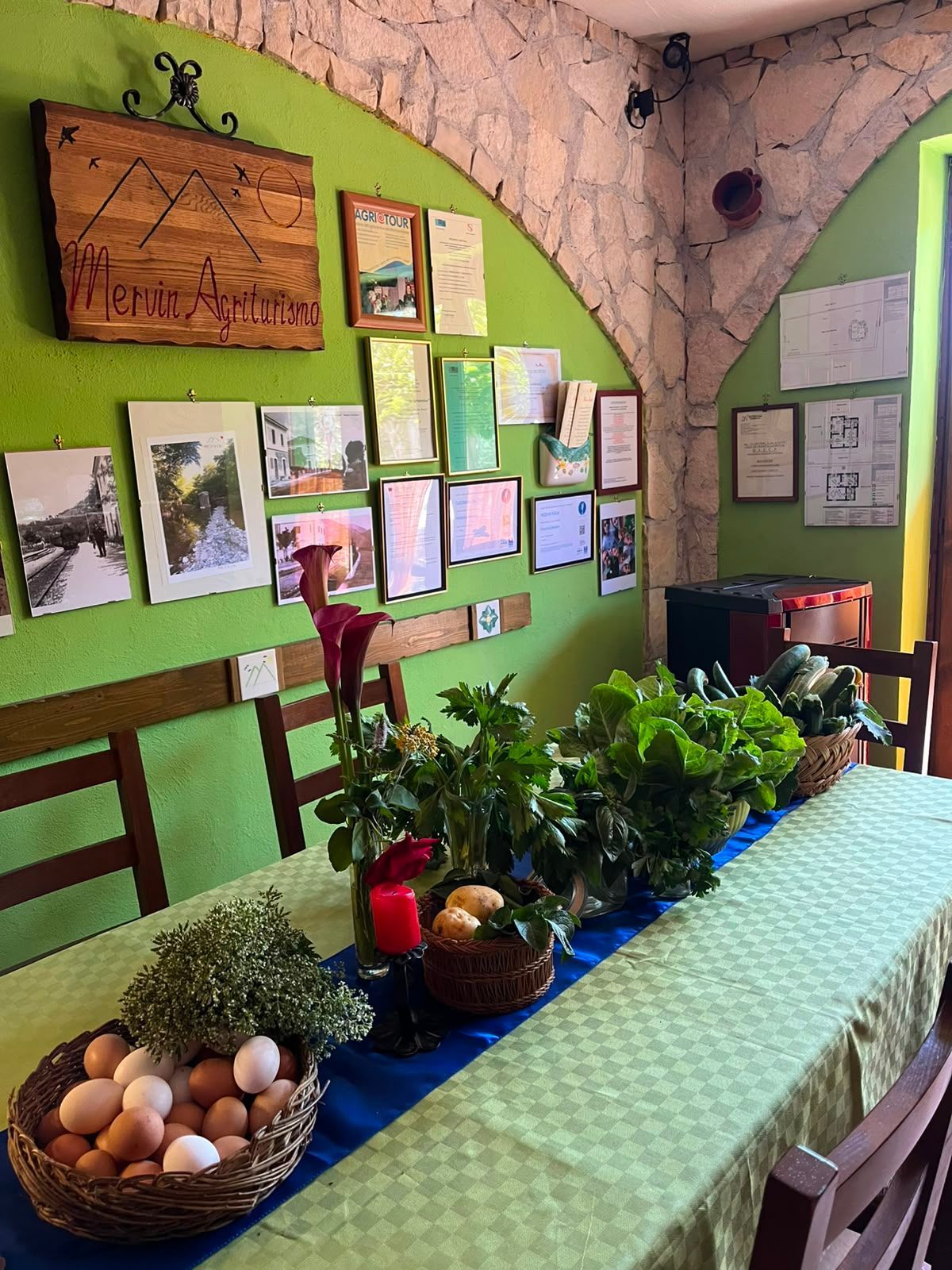 Tavolo verde con cestino di uova ed erbe aromatiche in una stanza rustica con foto e poster alle pareti.