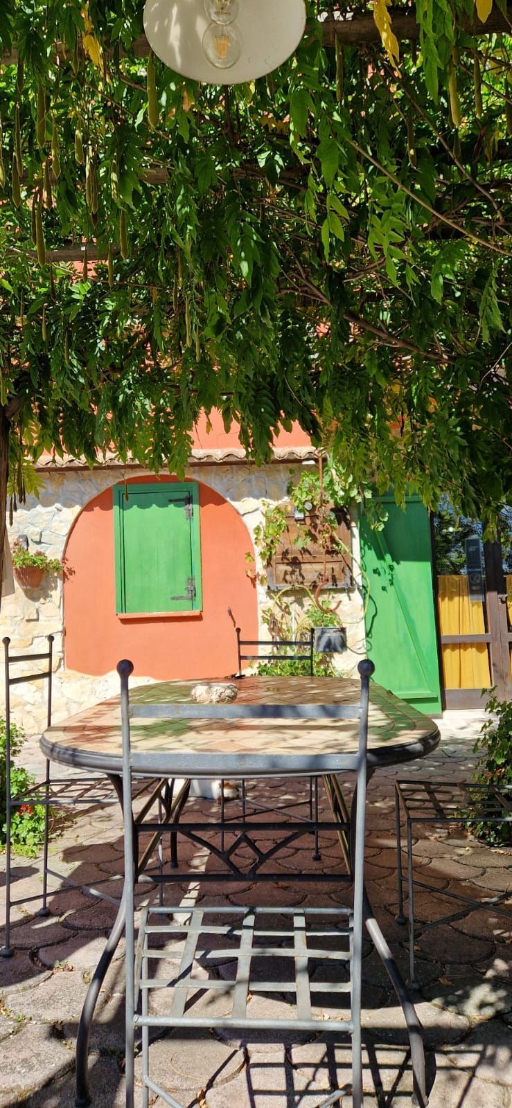 Tavolino da caffè all'aperto sotto alberi frondosi, di fronte a porte colorate e a un muro color pesca in un cortile soleggiato.