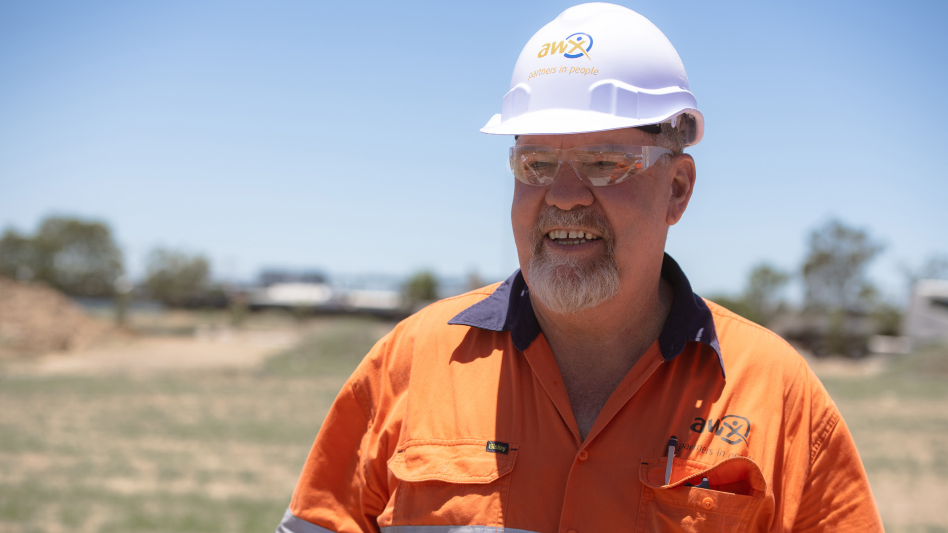 Man in orange workwear and hard hat smiles outdoors.