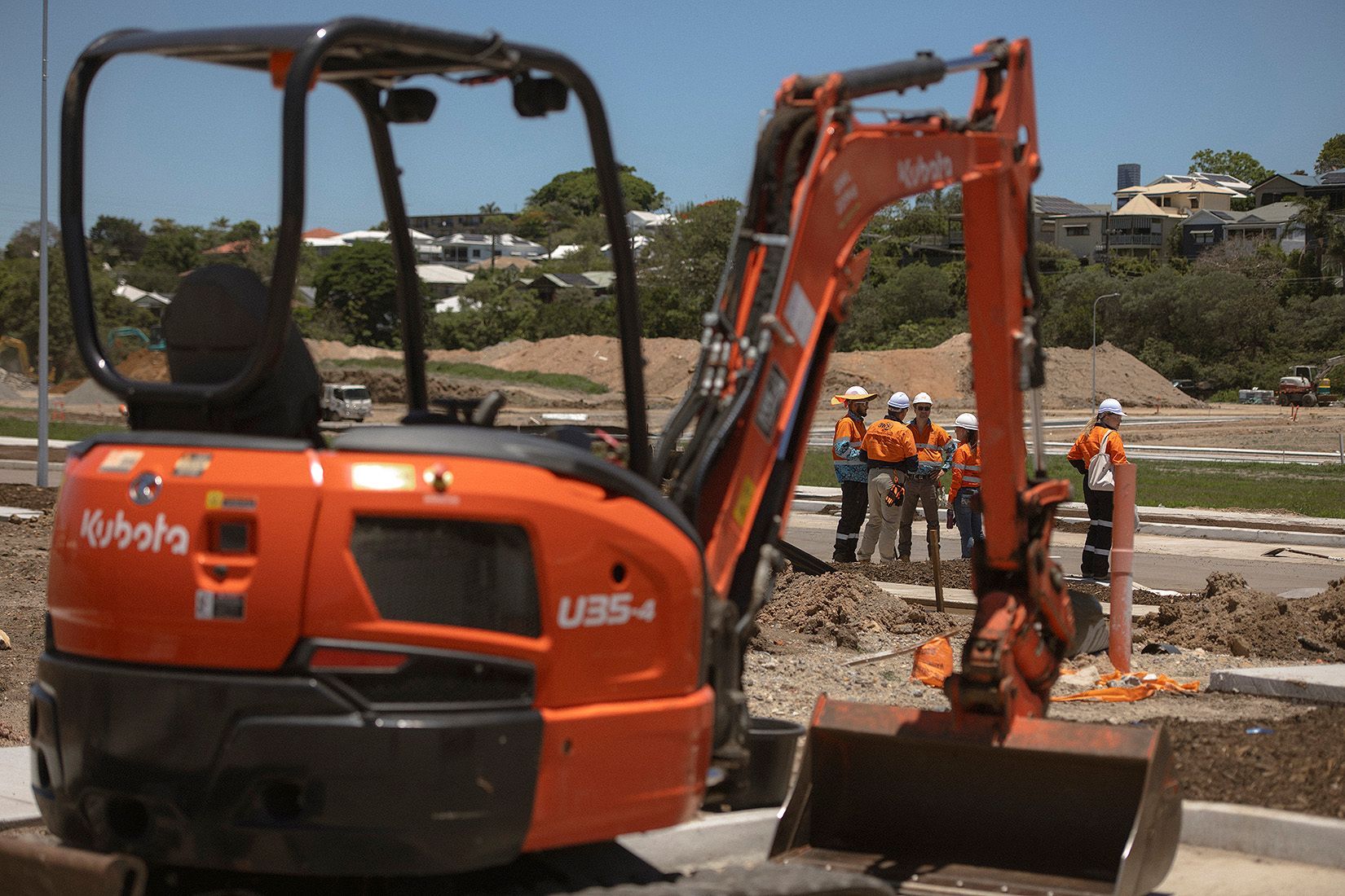 Orange excavator with workers on a roadside construction site outdoors