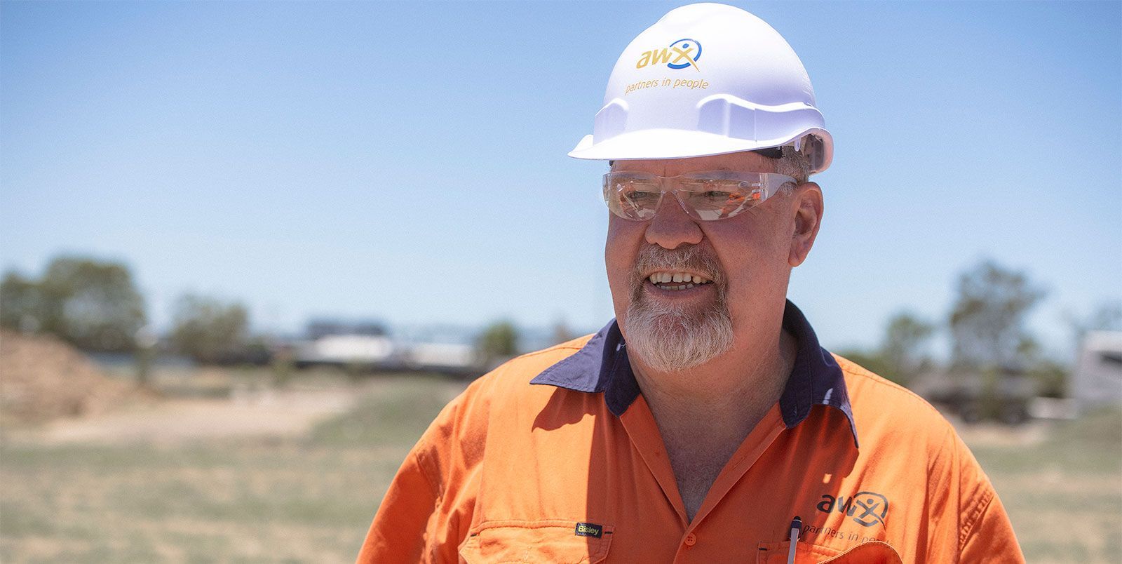 Man in orange workwear and hard hat smiles outdoors.