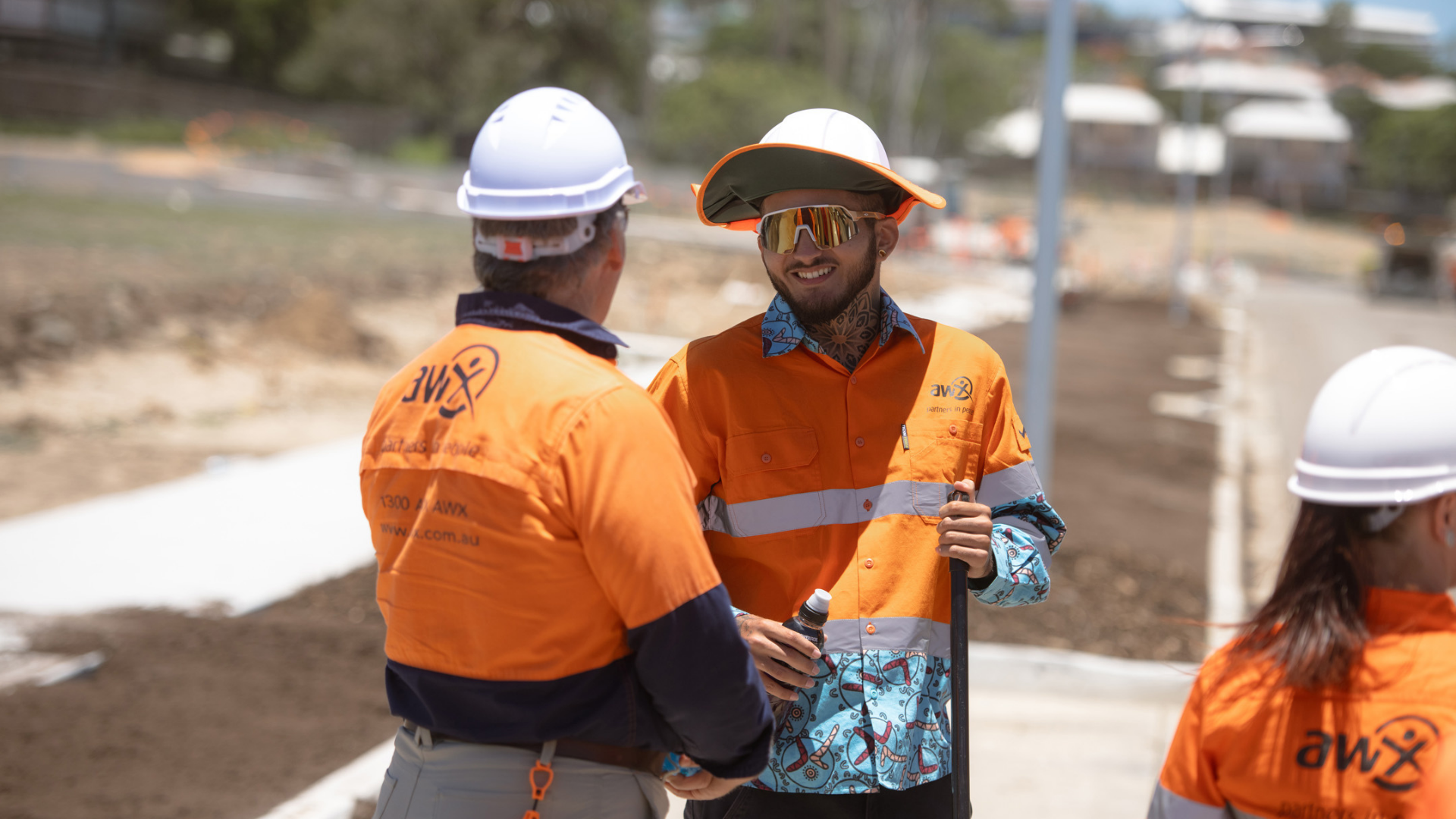 Construction workers in orange safety shirts and hard hats talking on a road site.