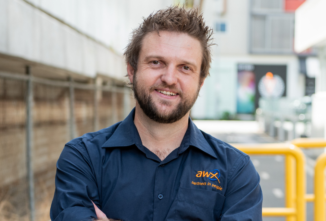 Smiling man in a navy work shirt standing outdoors near yellow railings