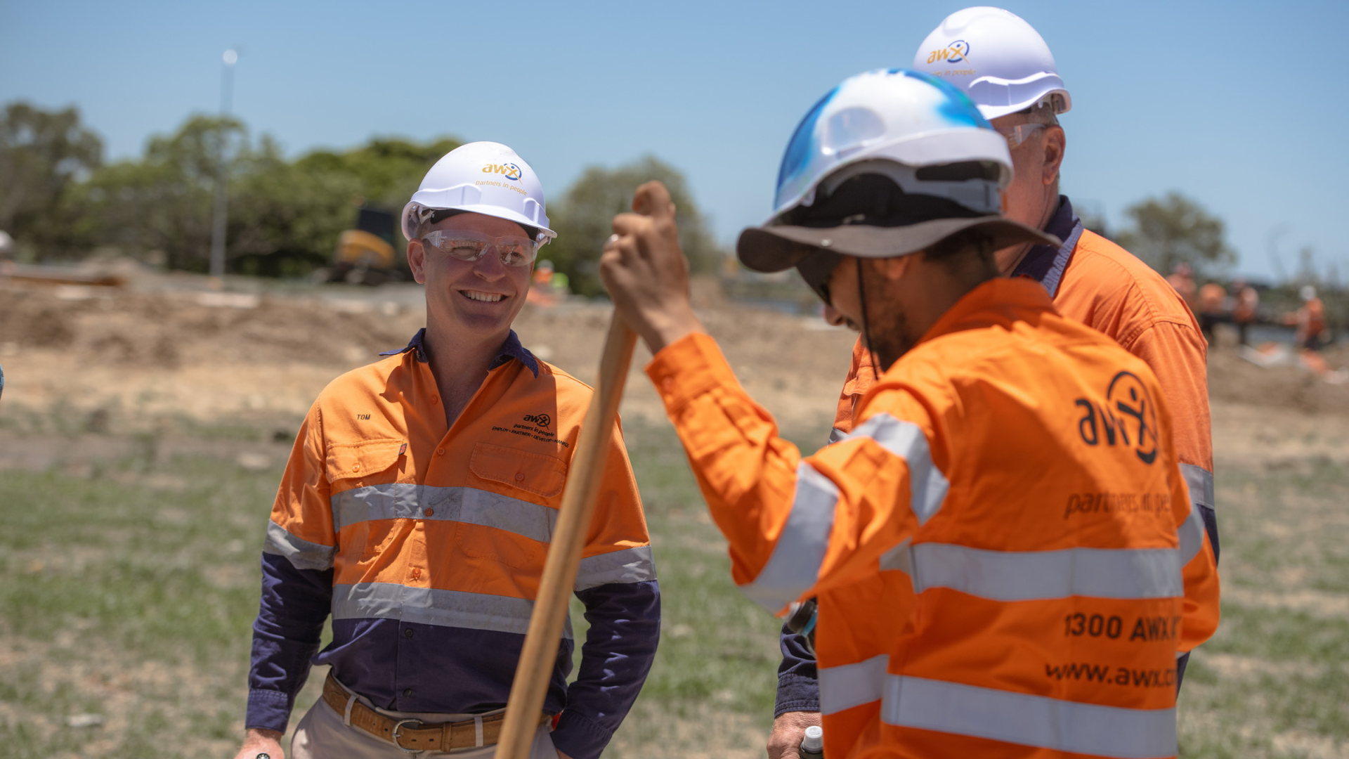 Three people in orange workwear on a construction site. One holds a shovel.