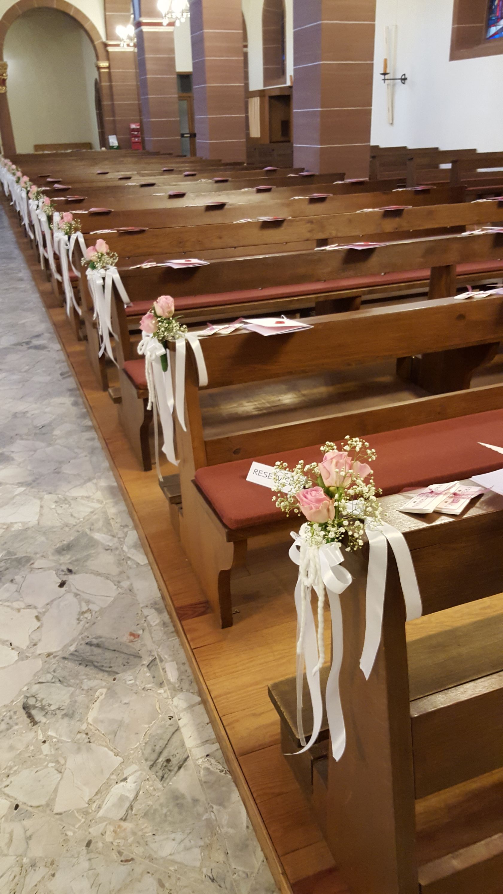 Eine Reihe von Holzbänken in einer Kirche, die mit Blumen und Bändern geschmückt sind.