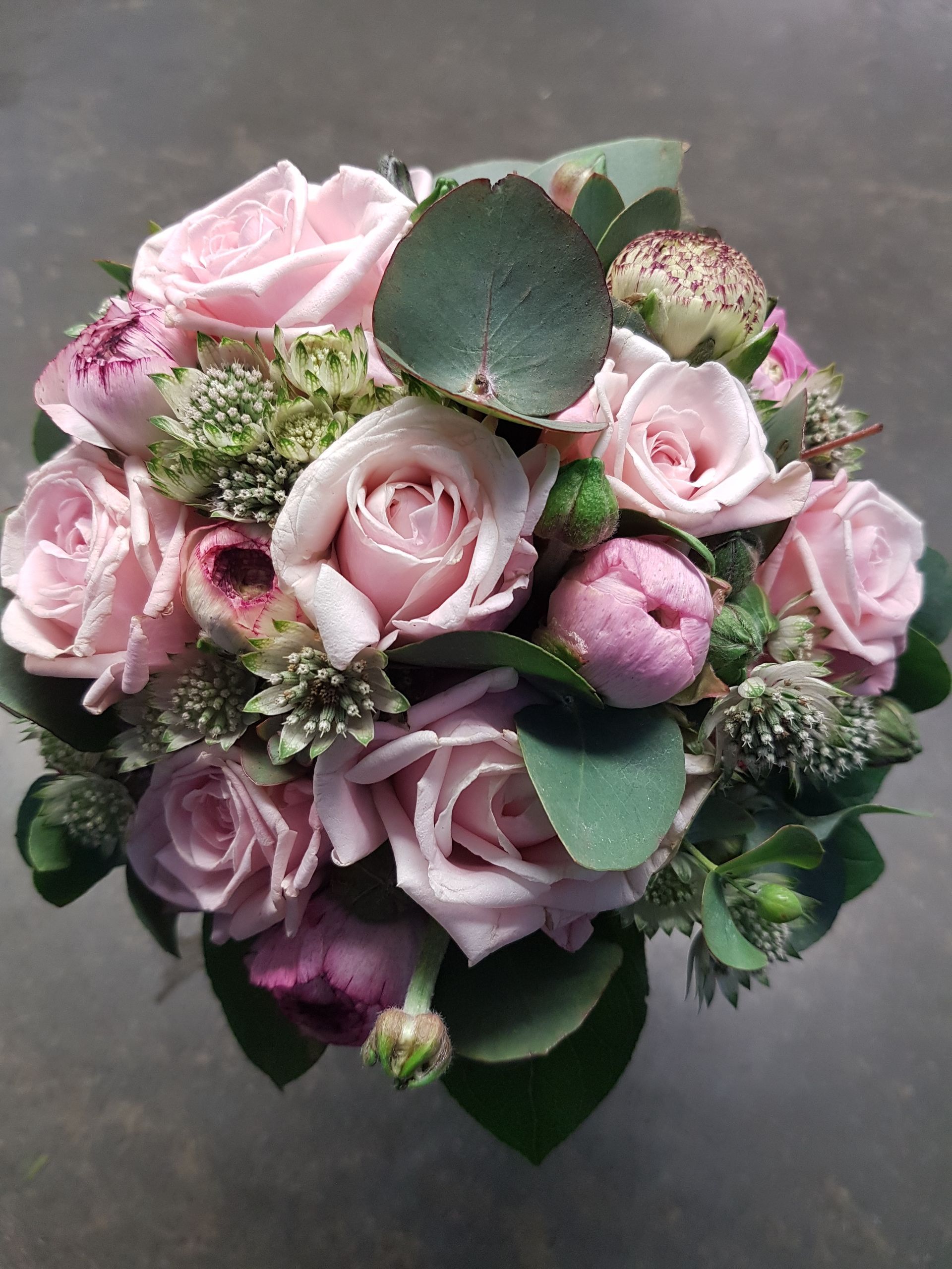Auf einem Tisch steht ein Strauß rosa Rosen und Grünpflanzen.