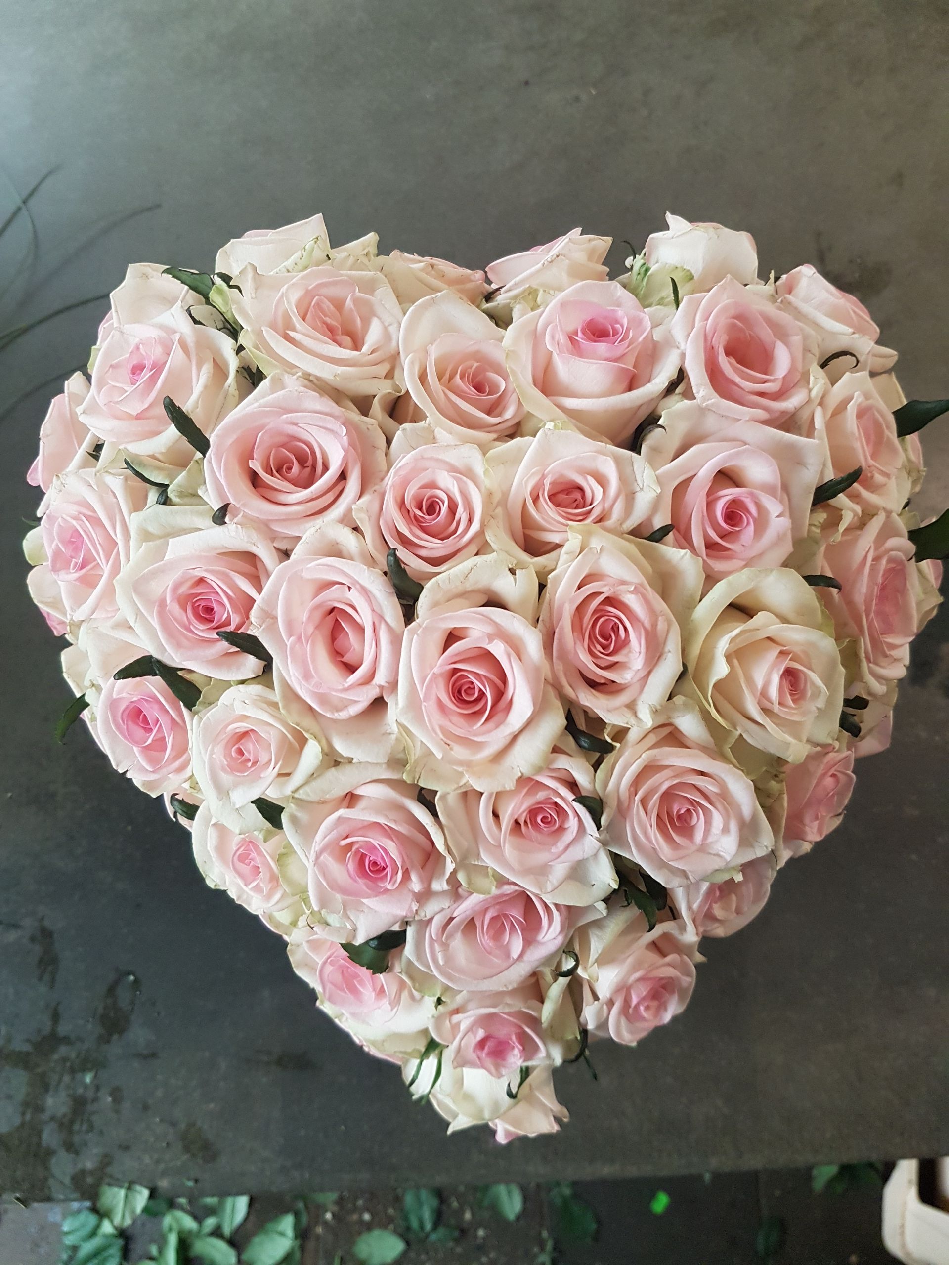 Auf einem Tisch steht ein herzförmiger Strauß rosa Rosen.