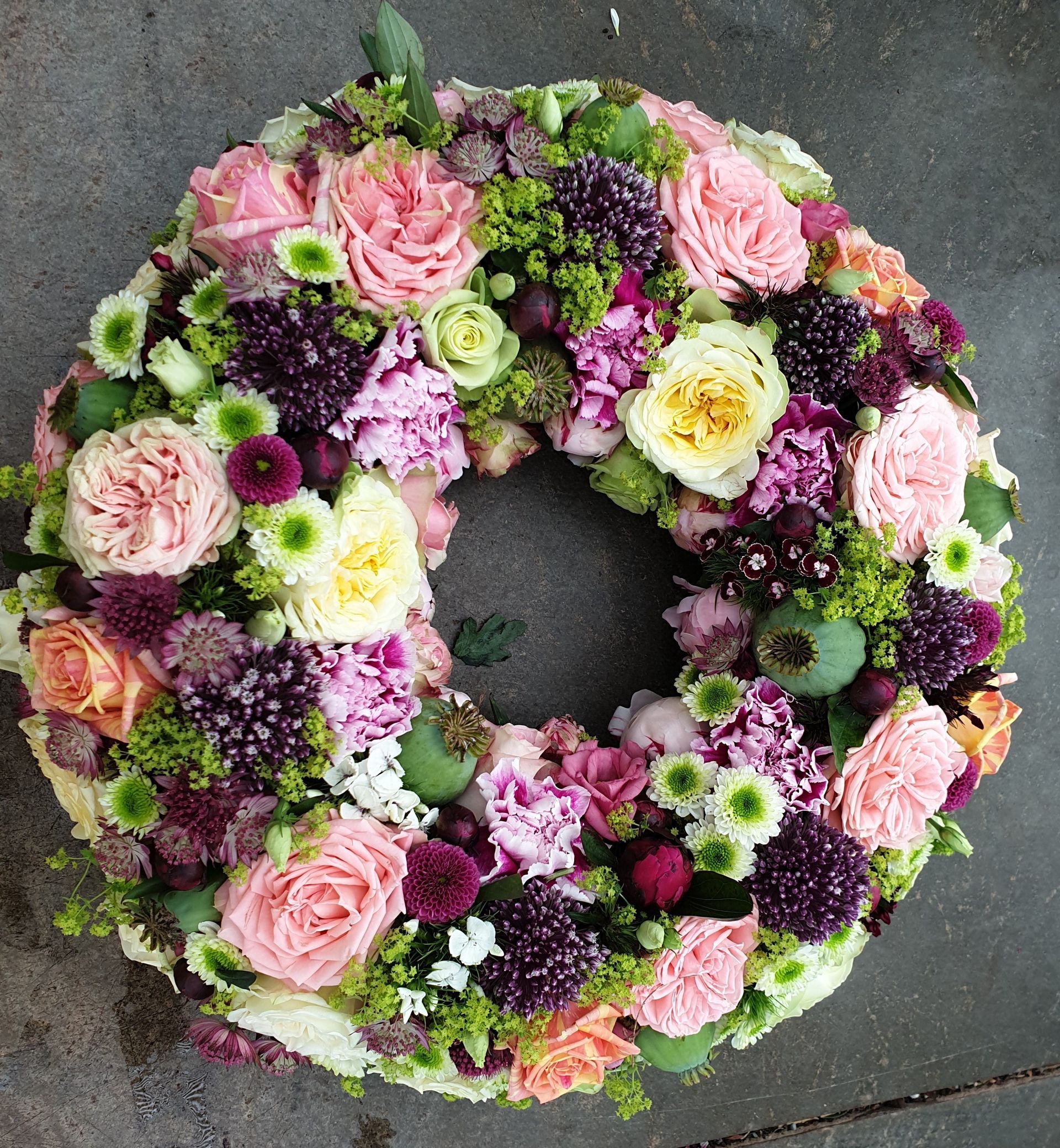 Auf einer Betonfläche liegt ein Kranz aus rosa und violetten Blumen.