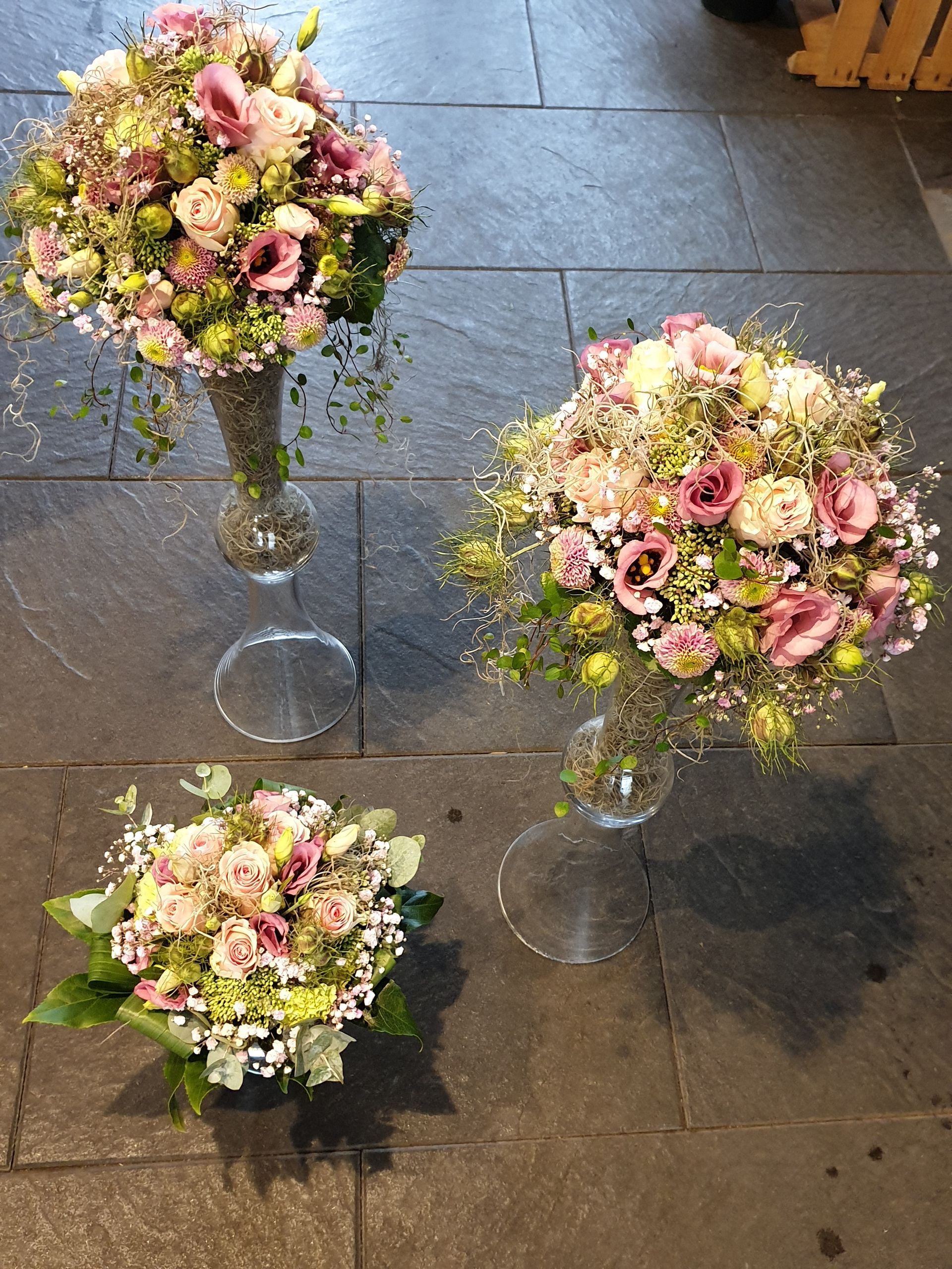 Drei mit Blumen gefüllte Vasen stehen auf einem gefliesten Boden.