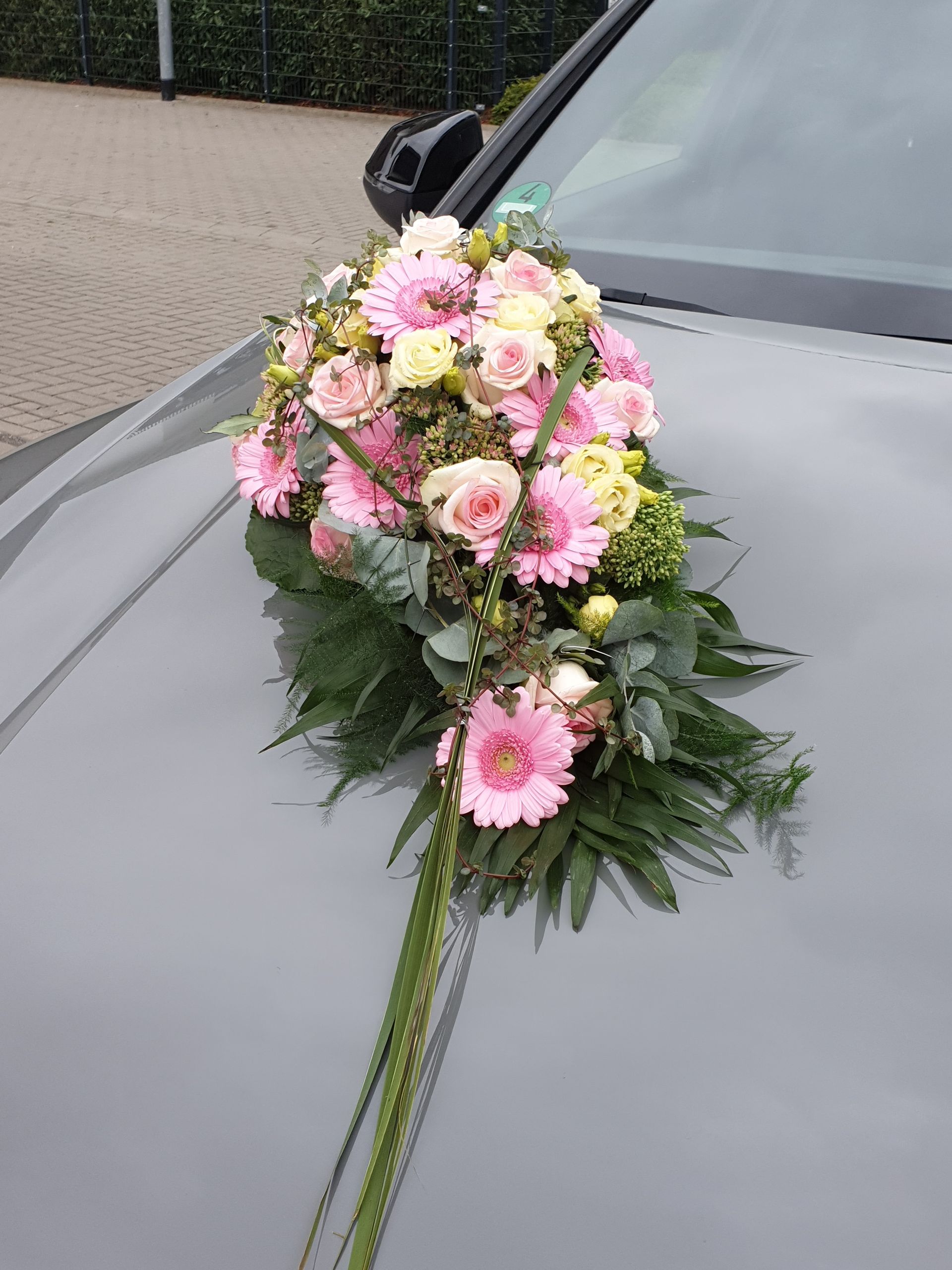 Auf einem Parkplatz steht ein Auto mit Blumen auf der Motorhaube.