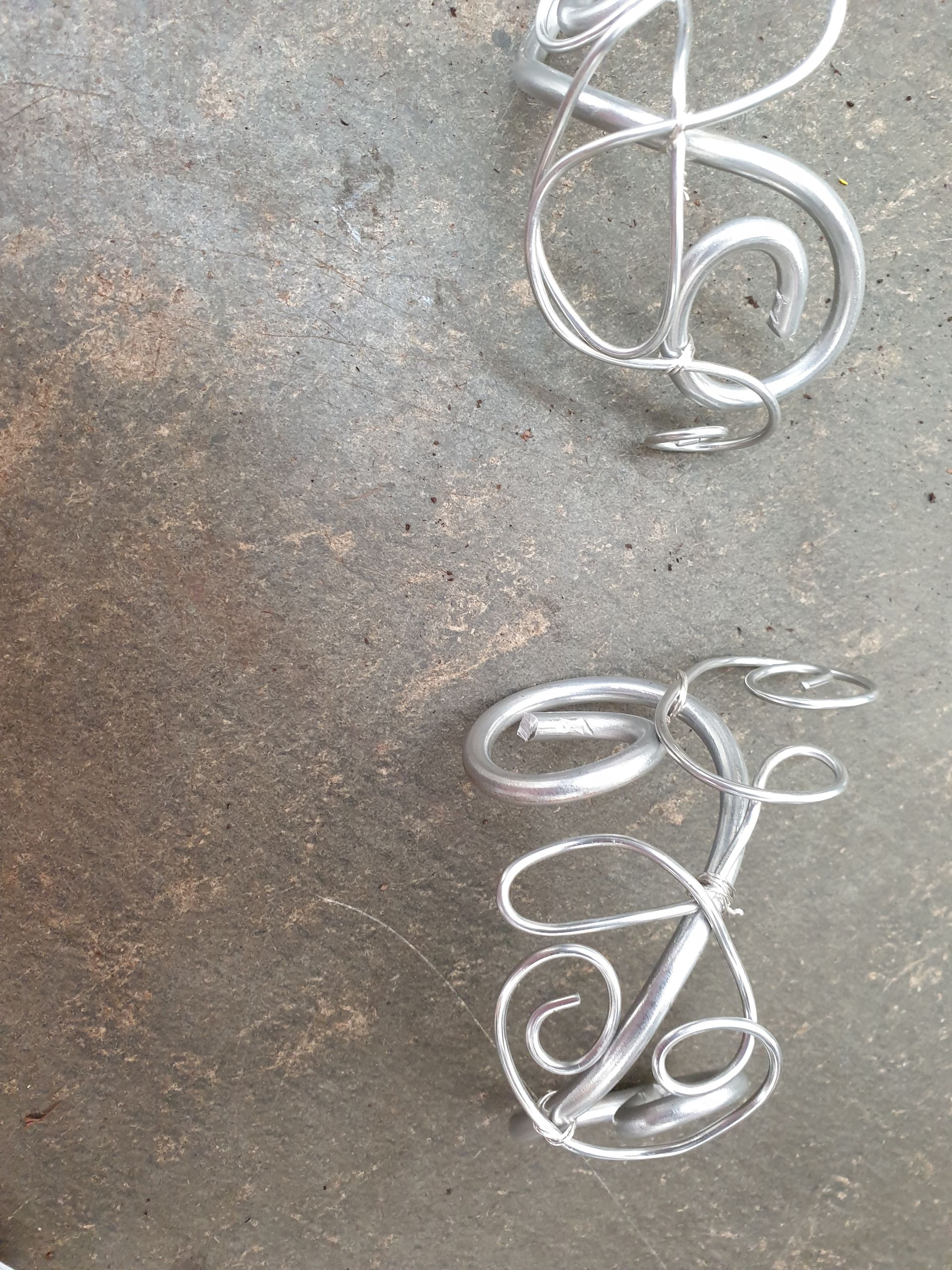 Ein Paar Armbänder aus Silberdraht liegen auf einer Betonoberfläche.
