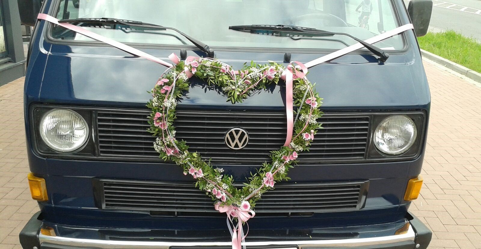 Ein blauer Lieferwagen mit einem herzförmigen Kranz auf der Motorhaube.
