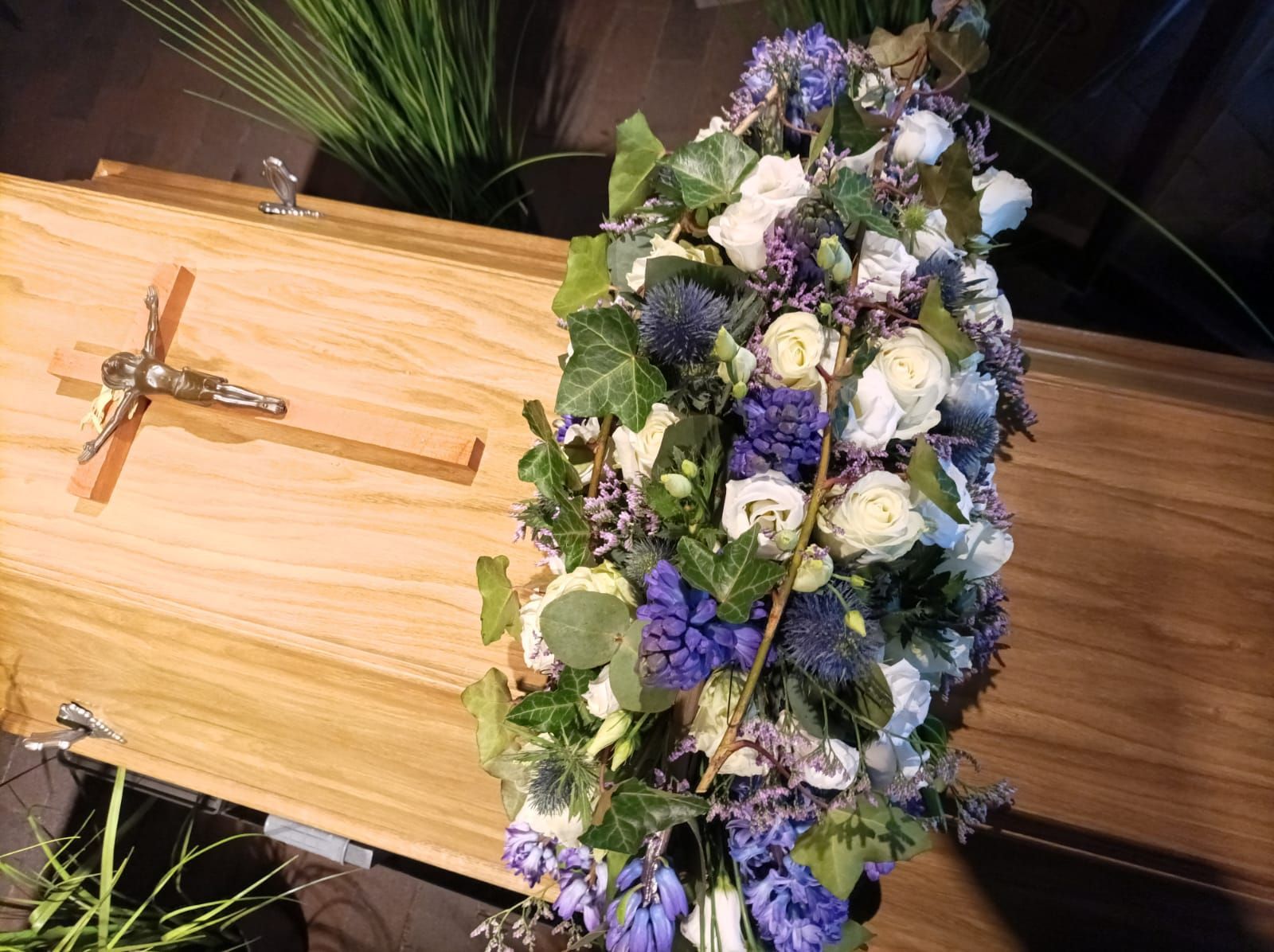 Ein Holzsarg mit violetten und weißen Blumen und einem Kreuz darauf.