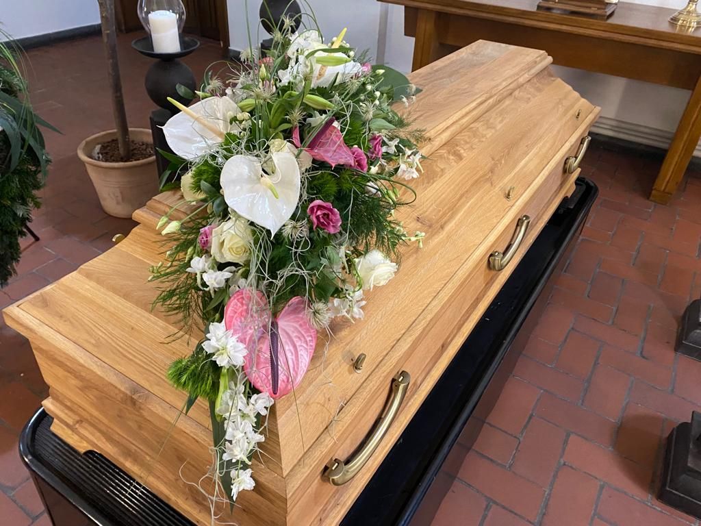 Ein Holzsarg mit Blumen darauf in einer Kirche.