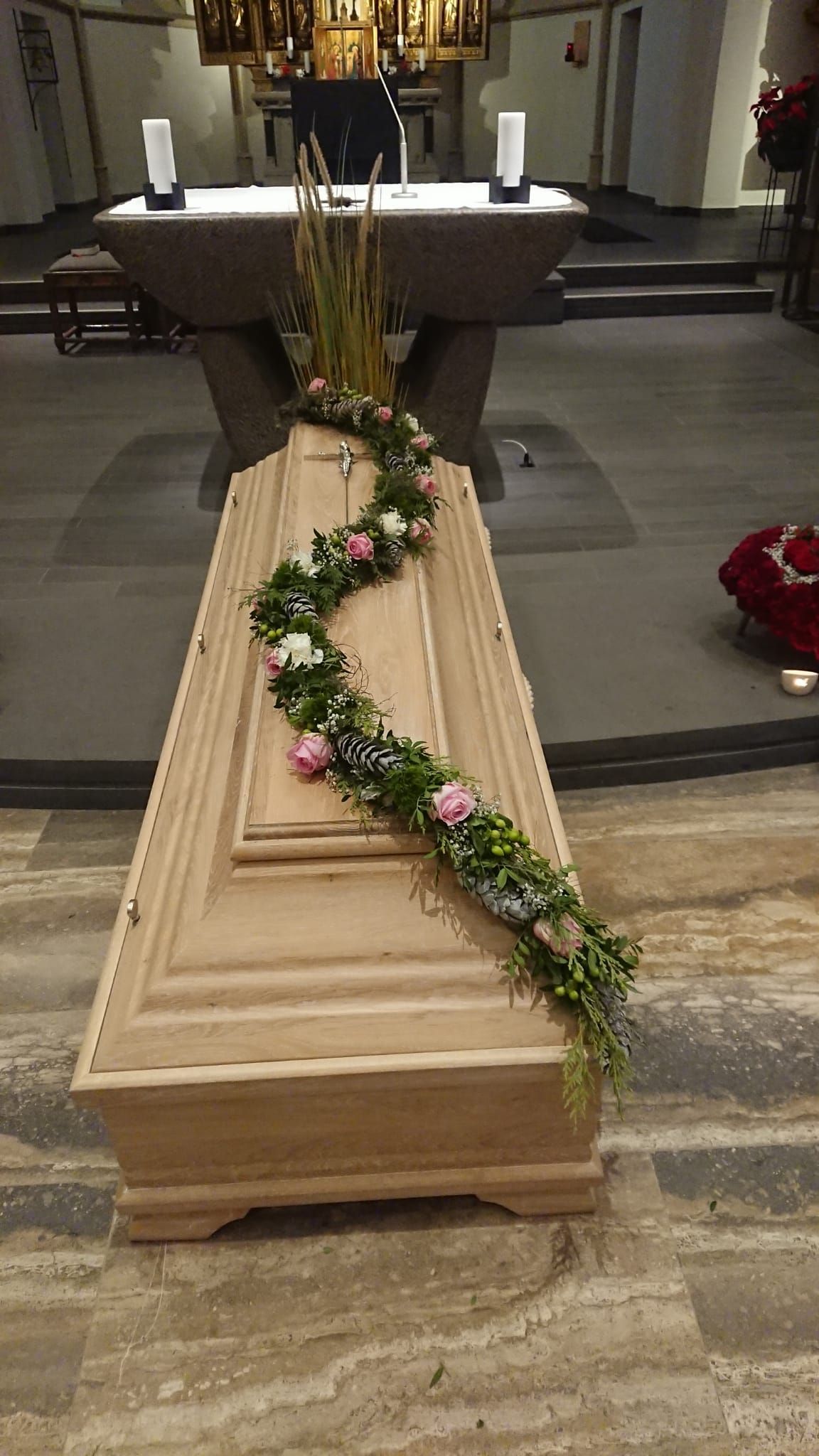 In einer Kirche ist ein Holzsarg mit Blumen geschmückt.