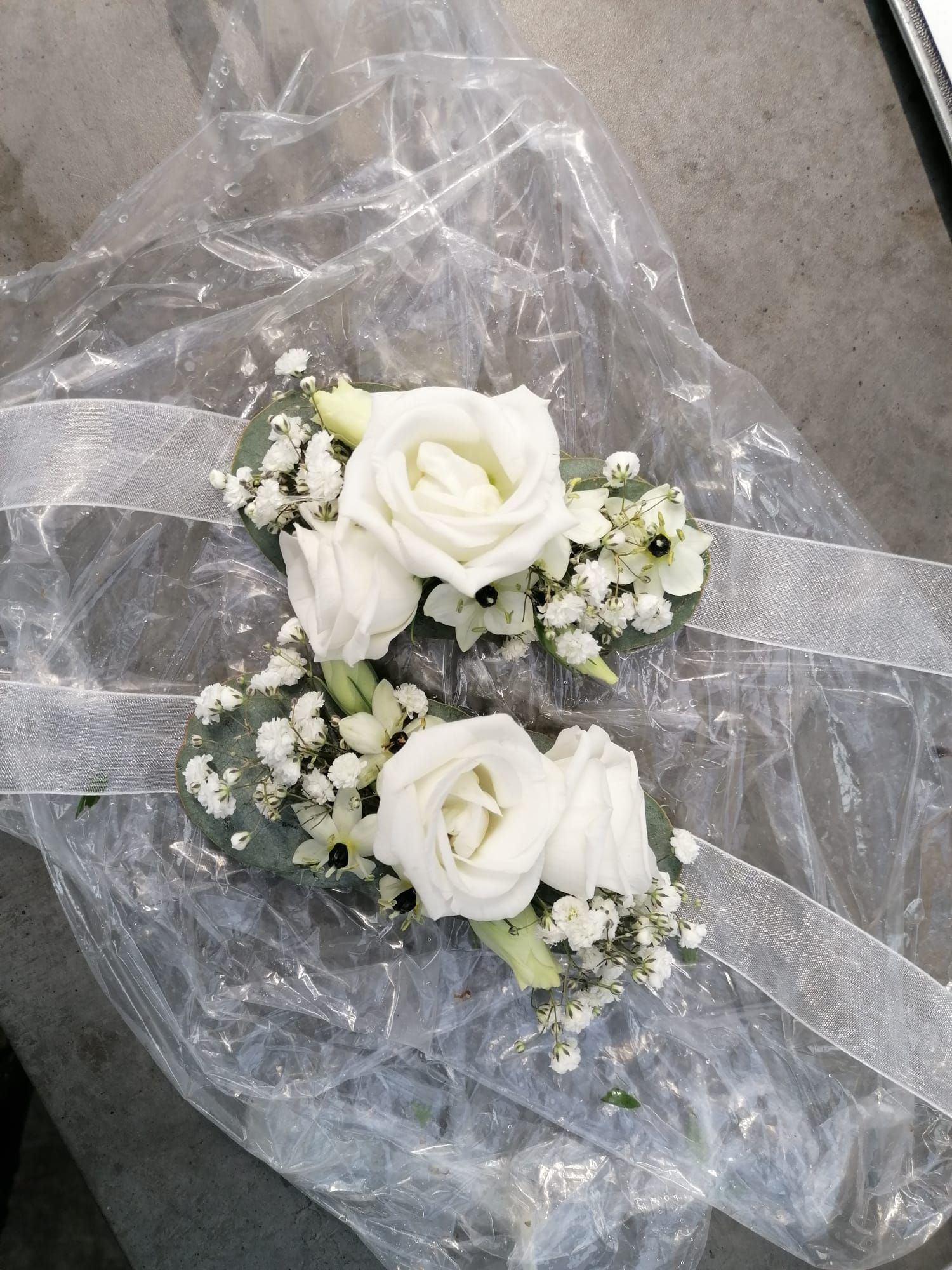 Eine Nahaufnahme eines Armbandes mit weißen Rosen und Schleierkraut.