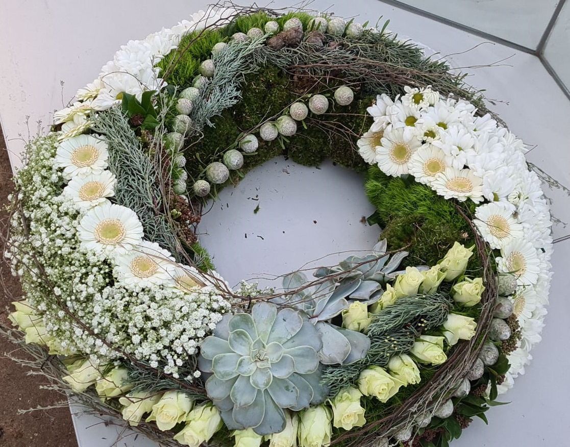 Auf einem Tisch steht ein Kranz aus weißen Blumen und Grünpflanzen.